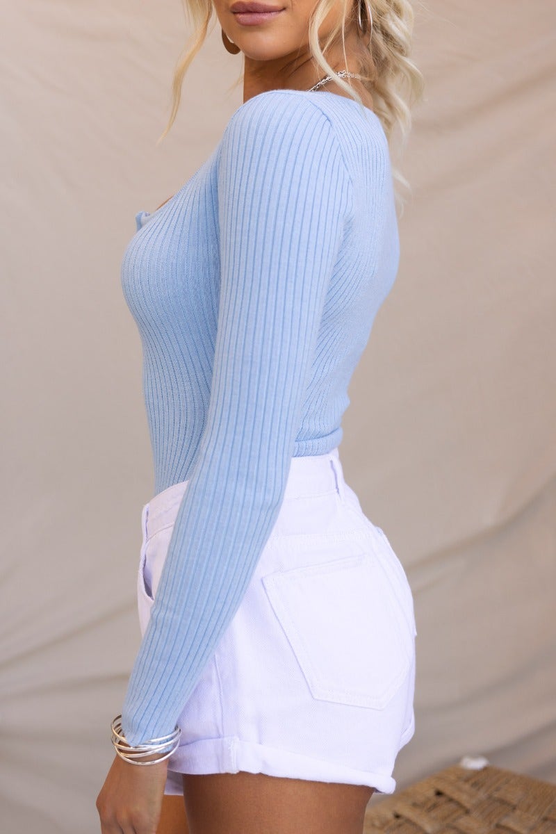 Model wearing Burke Bodysuit in light blue ribbed knit, scoop neckline, paired with white shorts.