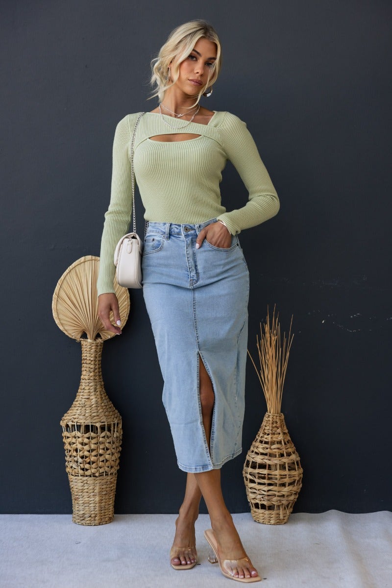 Model wearing Daia Top in ribbed knit with asymmetrical neckline and cut-out, paired with denim skirt.