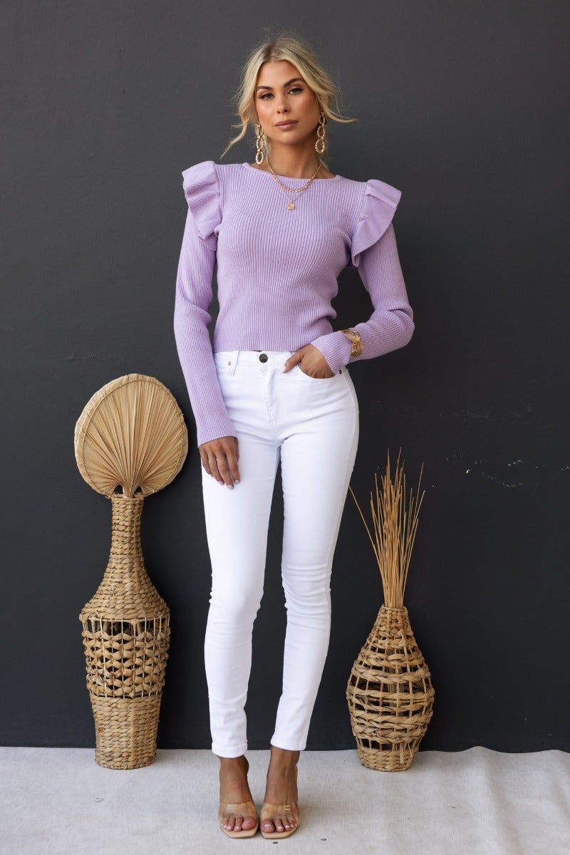 Woman wearing a lilac ribbed top with frill detail, paired with white jeans, styled with decorative baskets.
