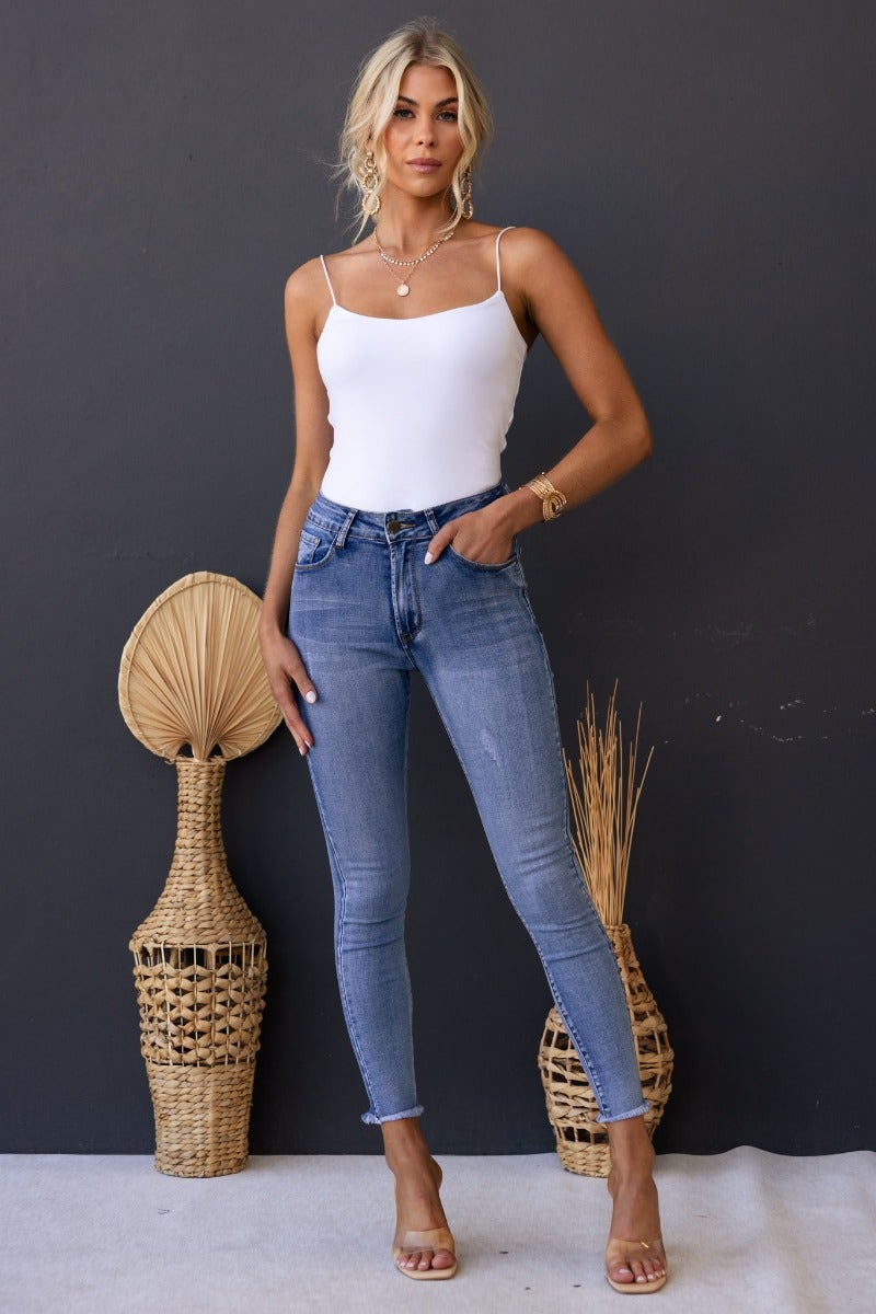 Model wearing Juicebox Jeans with mid waist, distressed details, and raw hem, paired with white top and beige heels.