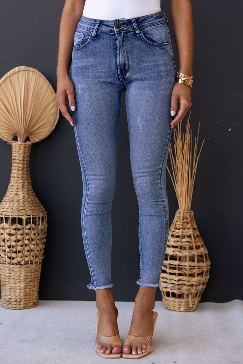 Model wearing Juicebox Jeans with mid waist fit, distressed details, and raw hem, showcasing a trendy skinny fit.