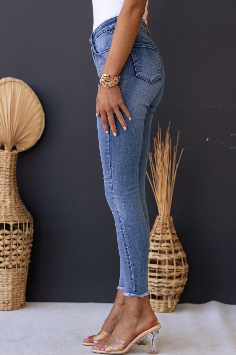 Model wearing Juicebox Jeans in mid waist fit with distressed details and raw hem against a dark background.