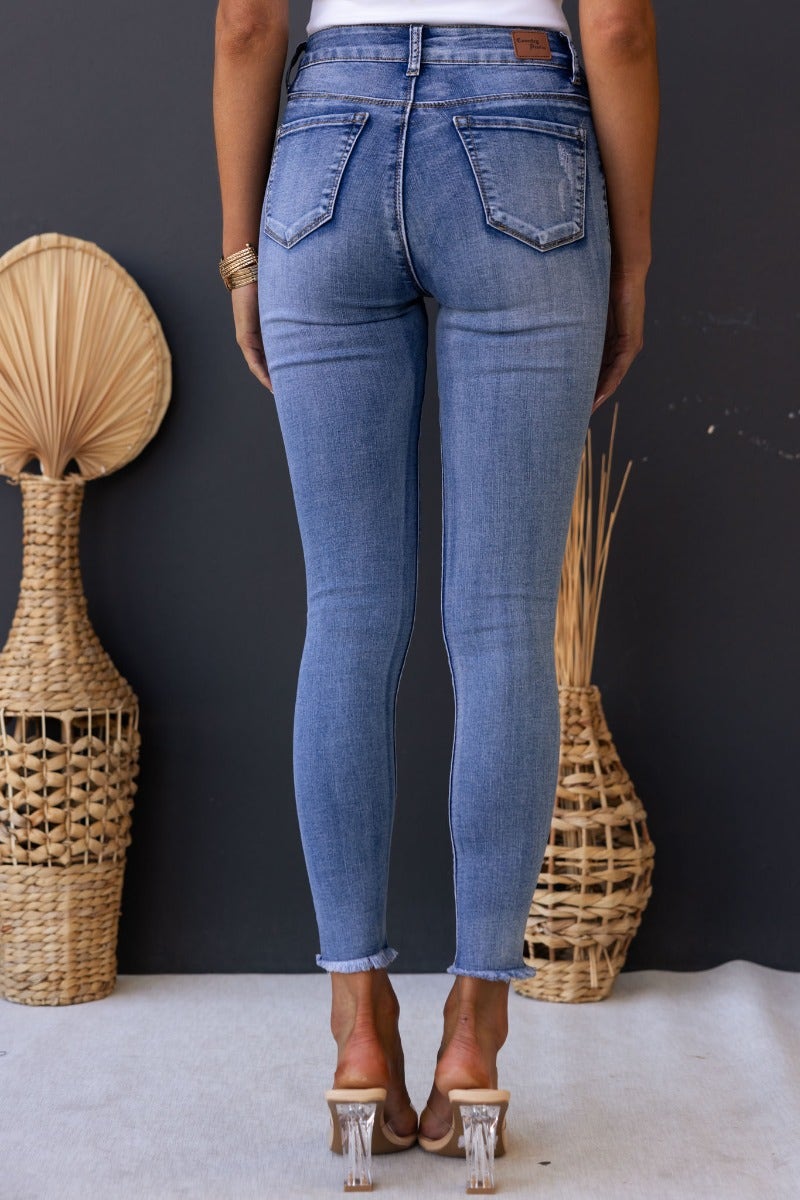 Back view of woman wearing Juicebox Jeans with a mid waist fit, raw hem, and distressed details.