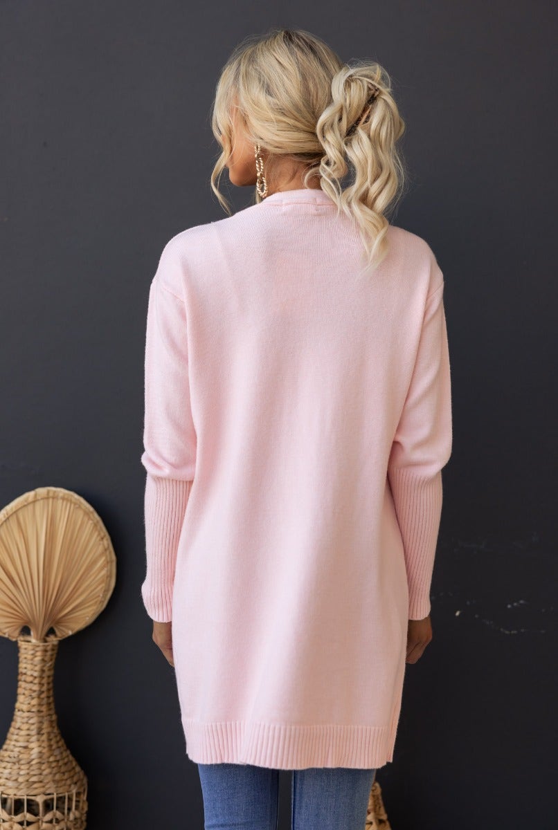 Back view of a model wearing a pink ribbed knit Hailey Cardigan, featuring a longline fit and front pockets.