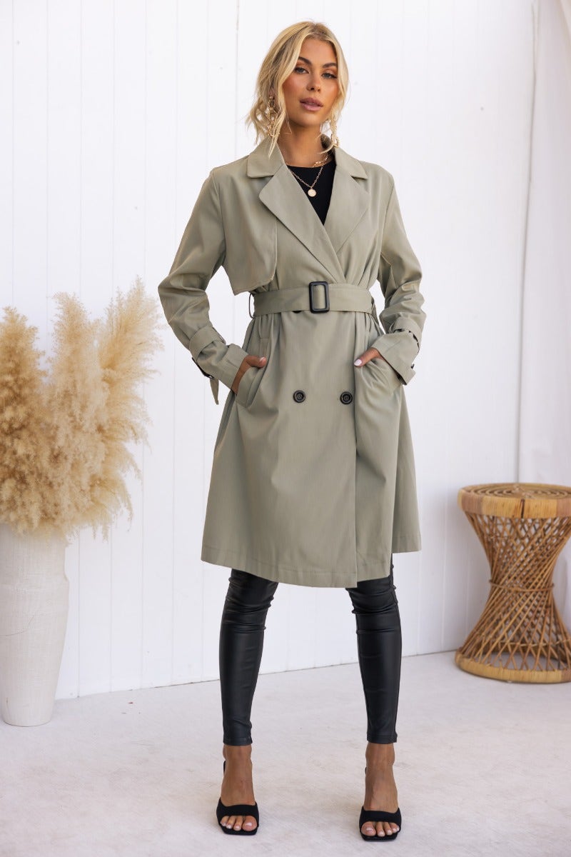 Stylish Cheyla trench coat in light green, featuring a removable belt and button closure, modeled with black leggings.