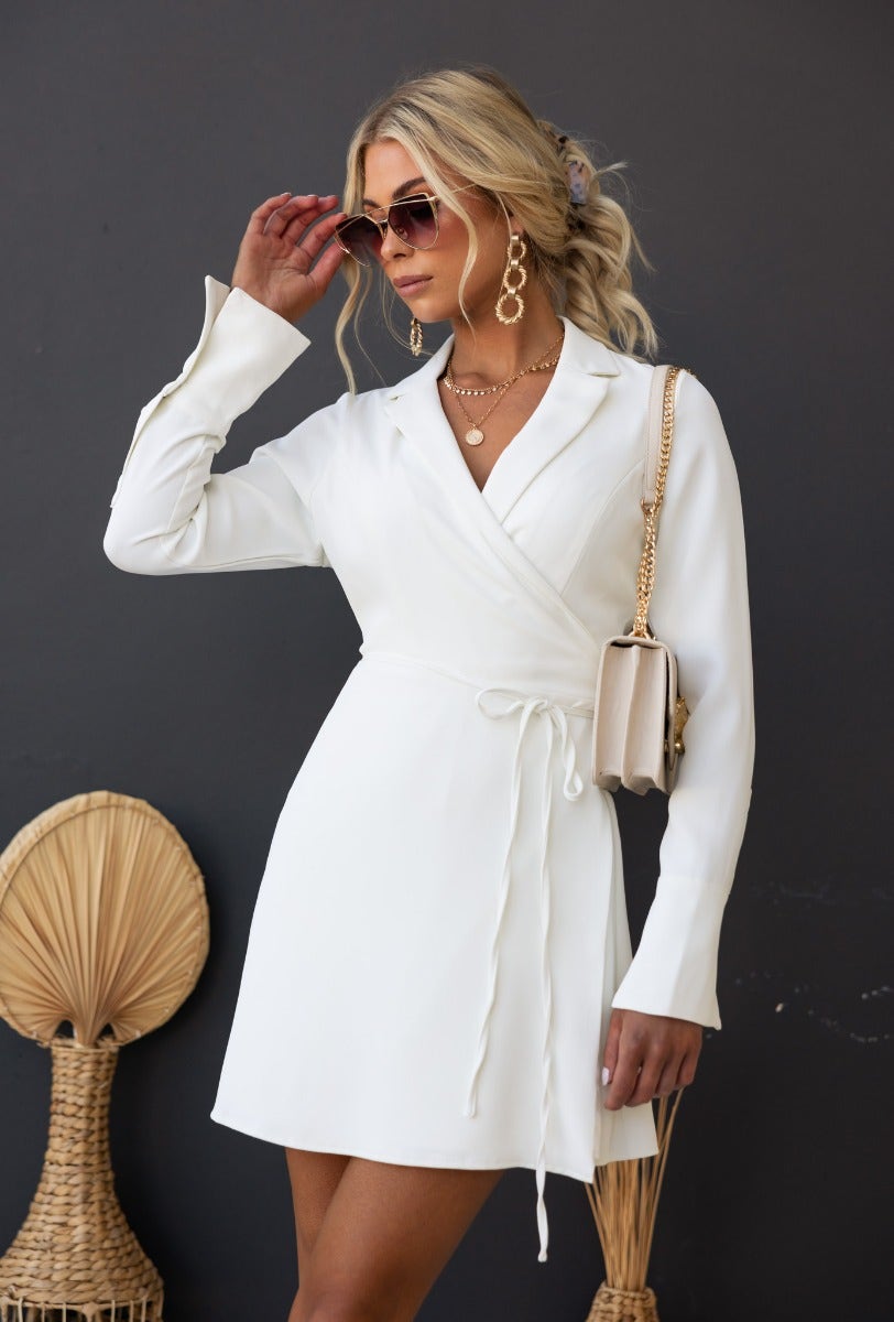 Valeria Wrap Dress in white with collar, fabric tie, and lined detail, styled by a model wearing sunglasses.