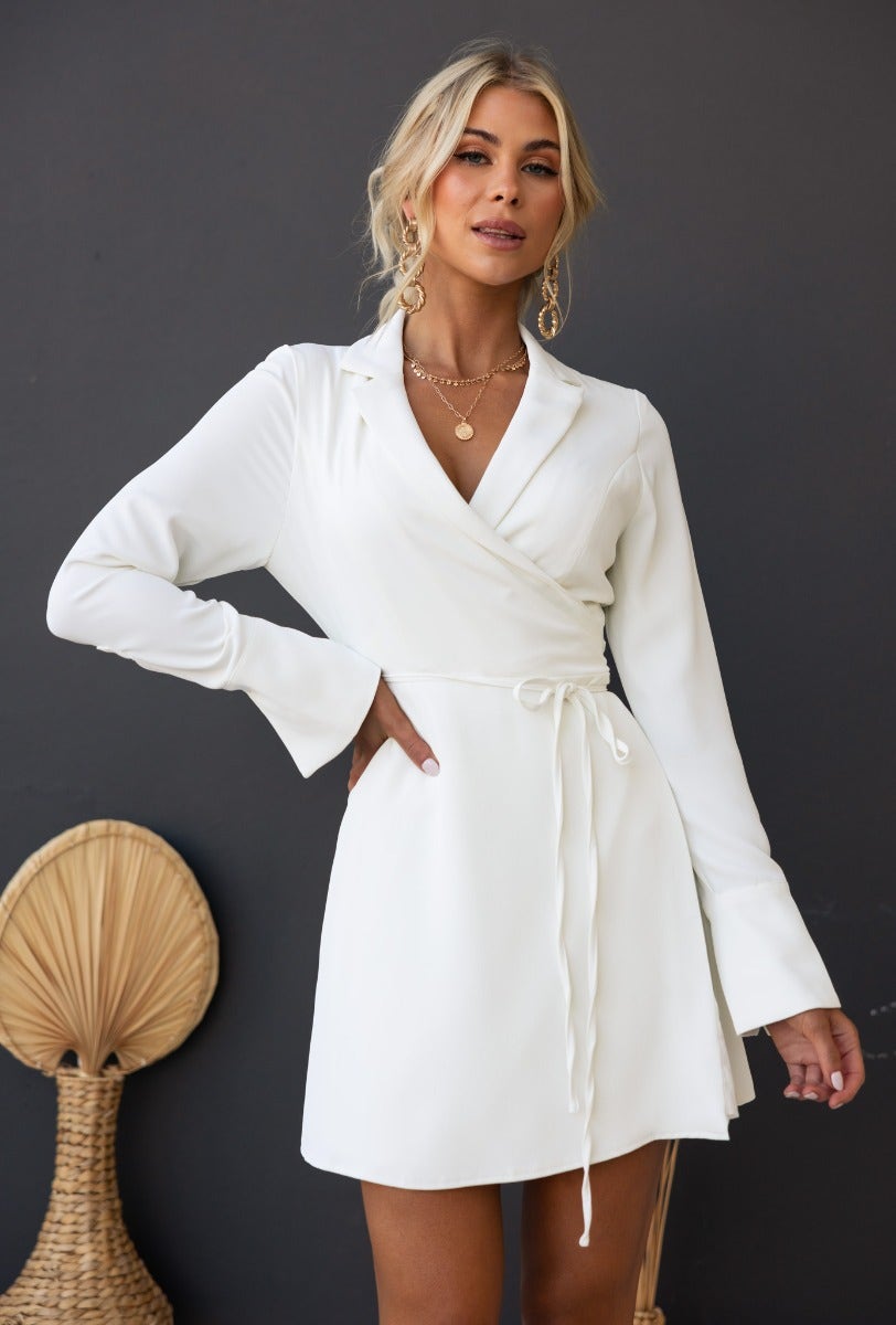 Valeria Wrap Dress in white, featuring a collar, fabric tie, and long sleeves, styled by model with neutral background.