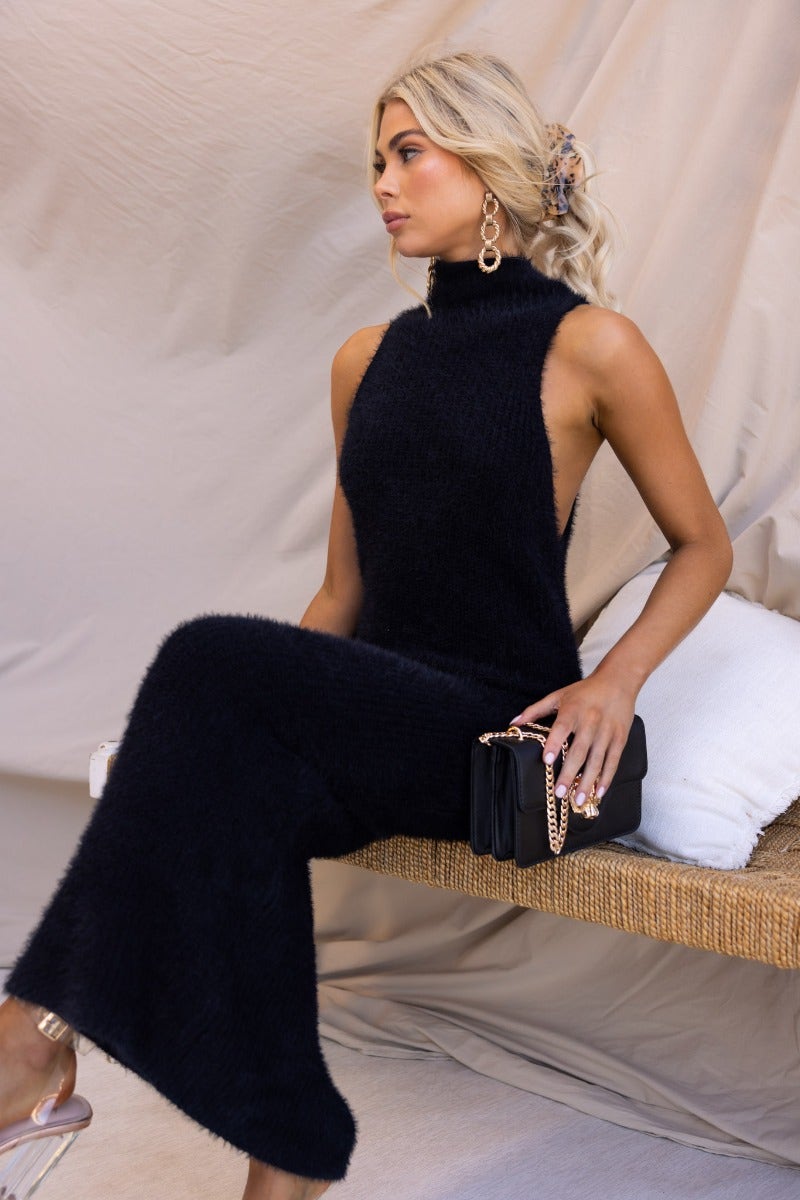 Model wearing a black fluffy knit maxi dress with a high neckline, styled with earrings and a handbag.