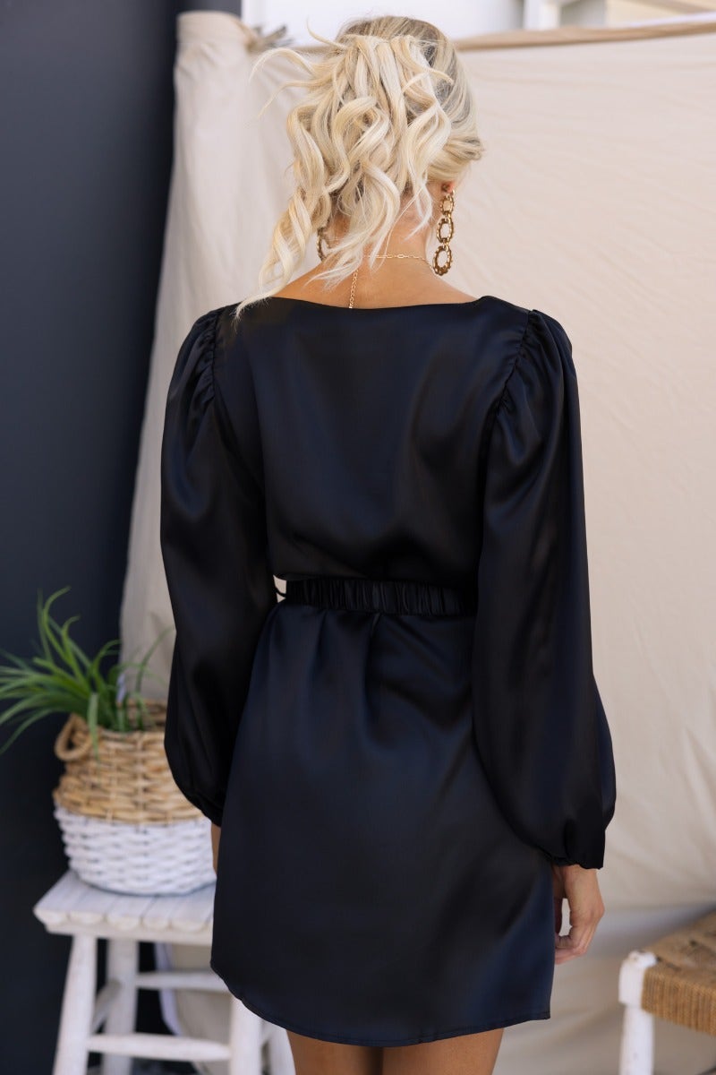 Model wearing Charli Dress, a black satin dress with elastic cuffs and a removable belt, showcasing the back view.