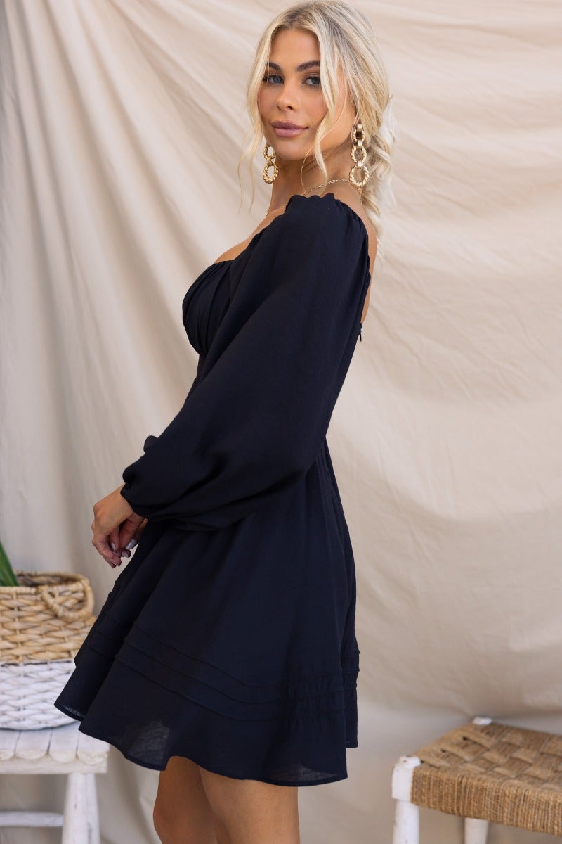 Model wearing the Amos Dress, a black dress with sweetheart neckline and elastic sleeves, styled with statement earrings.