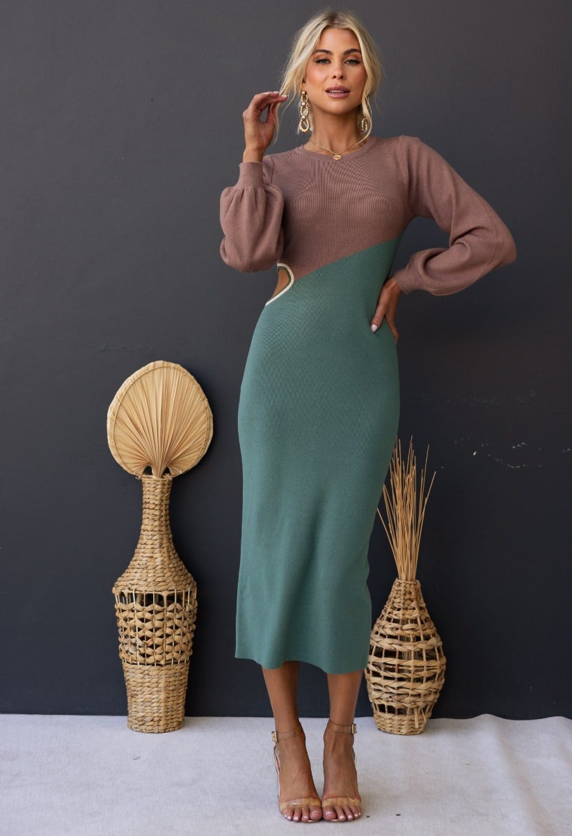 Torez Midi Dress in ribbed fabric featuring a round neckline, waist cut-out, and bishop sleeves, styled with minimalist accessories.