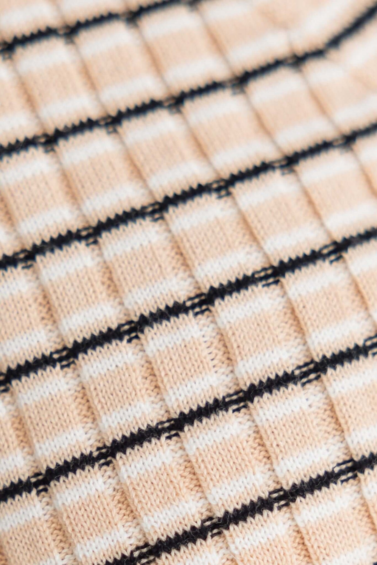 Close-up of textured peach knit fabric featuring a grid pattern with black and white stripes.