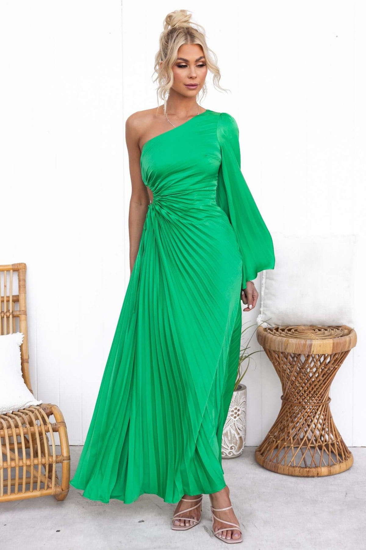 Woman in a vibrant green pleated maxi dress with one shoulder and cut-out waist, styled elegantly.