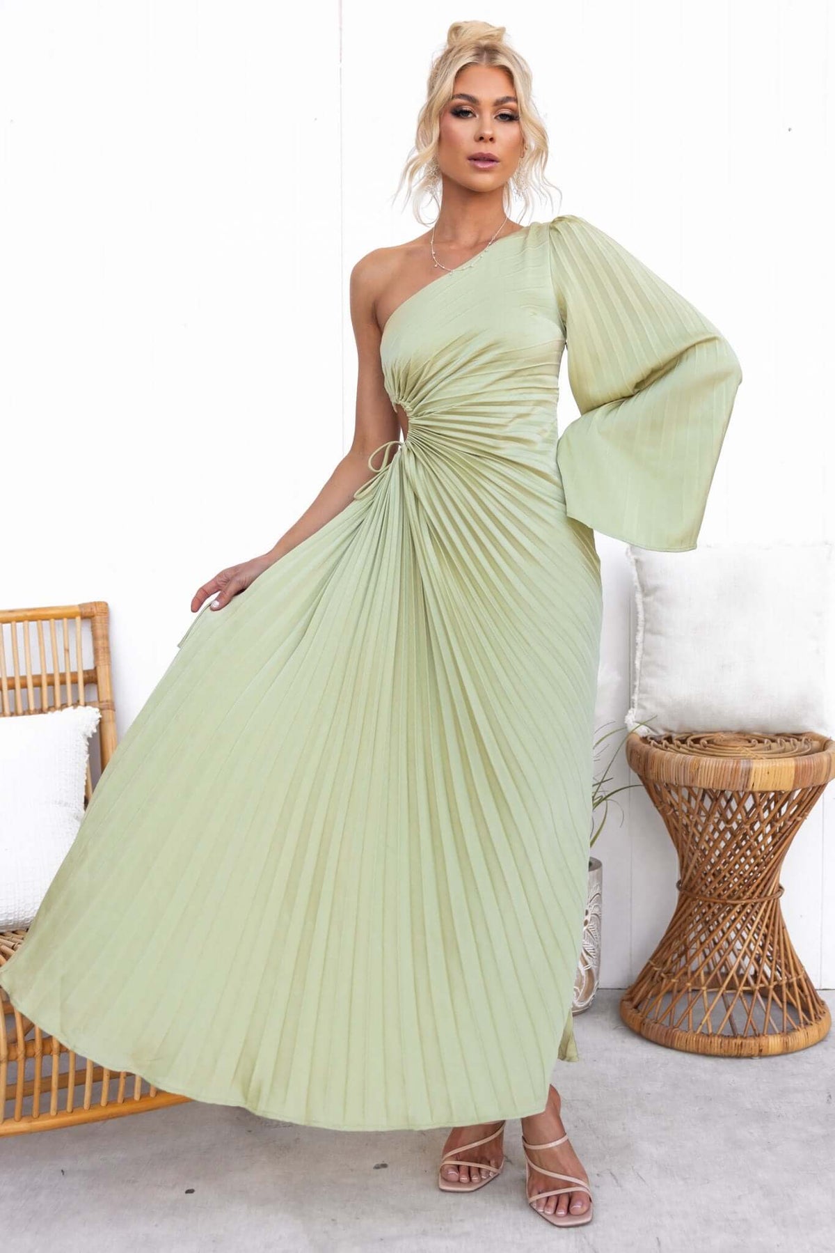 Model wearing a pleated one-shoulder maxi dress in soft green with a drawstring tie at the waist.