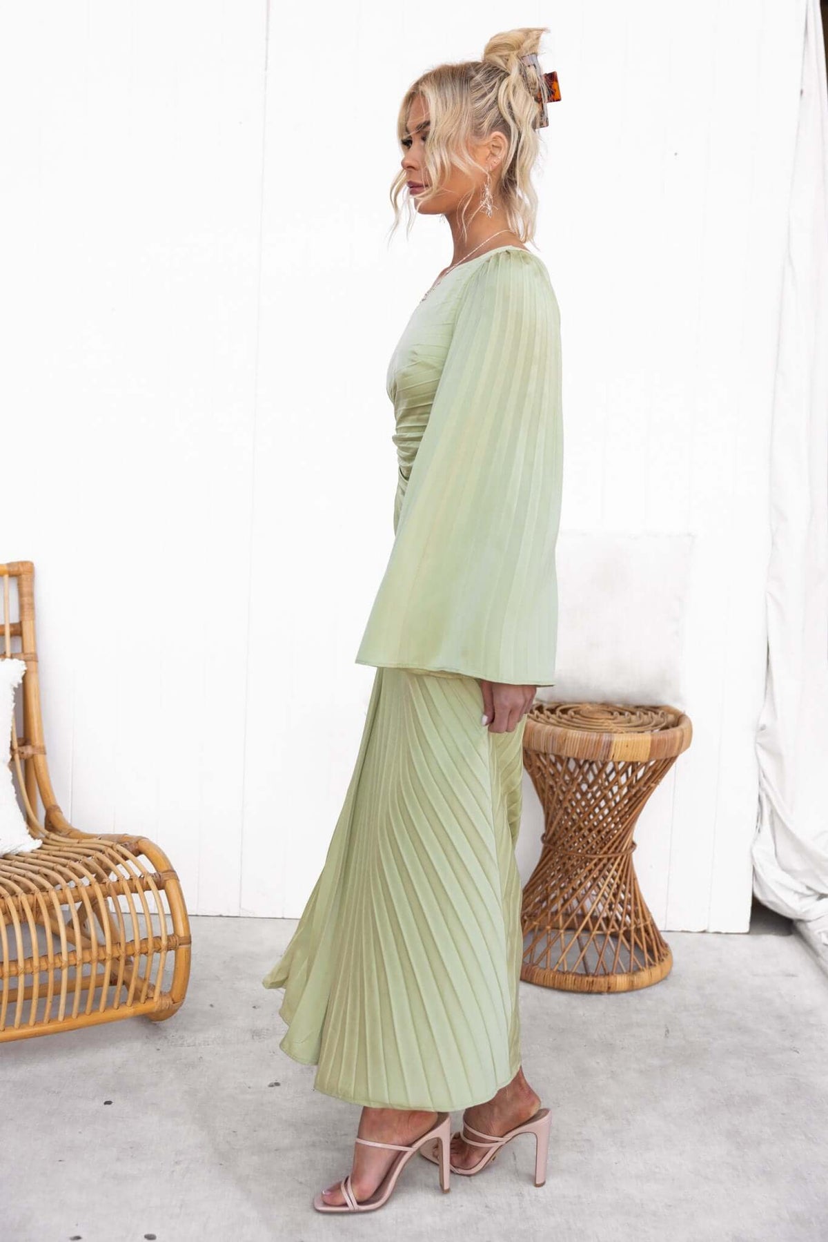 Model wearing a pleated one-shoulder maxi dress in soft green, showcasing cut-out waist detail and satin finish.