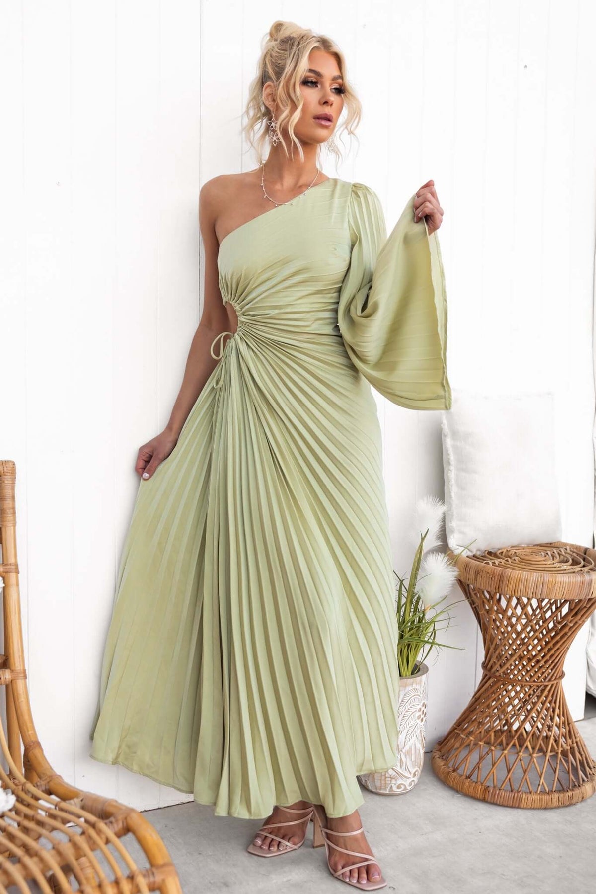 Model wearing a pleated one-shoulder maxi dress in light green, featuring a cut-out waist and satin finish.