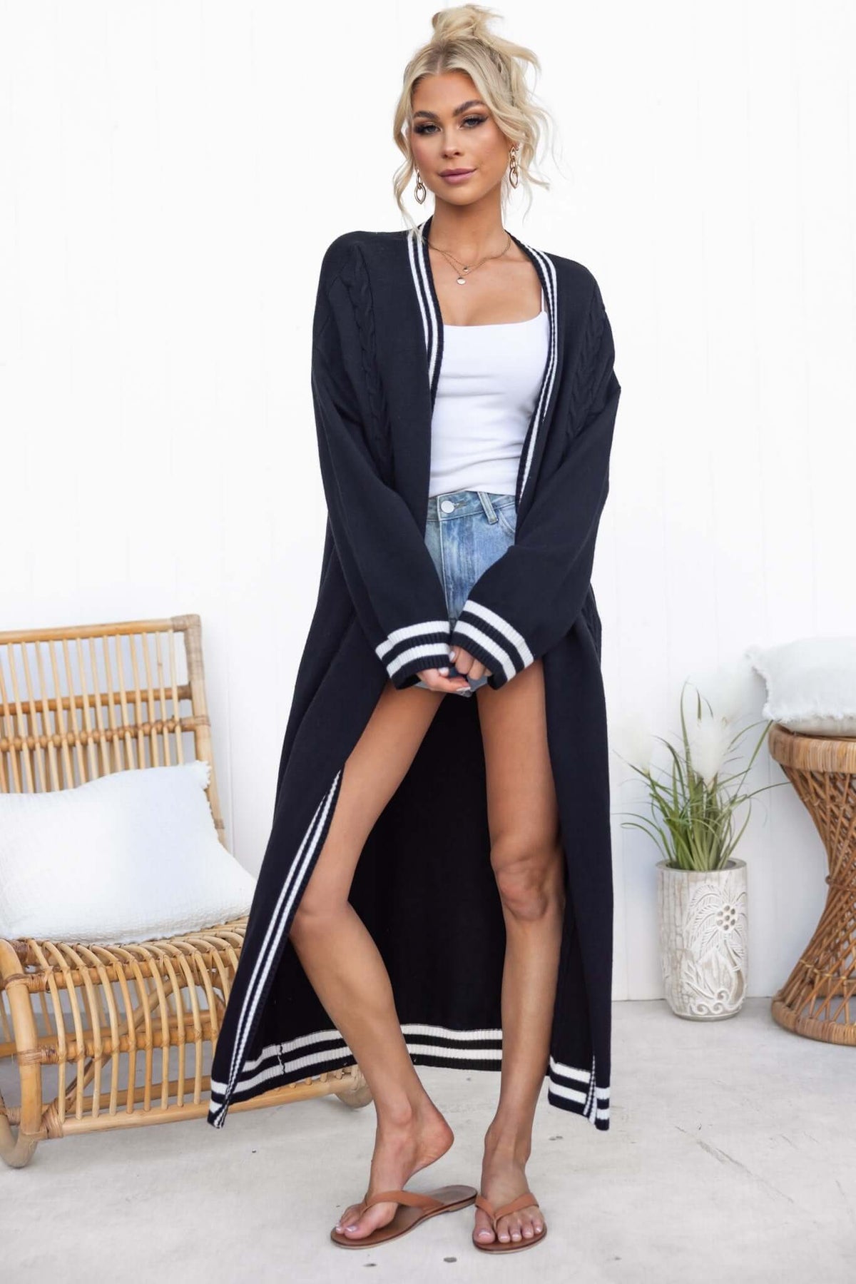 Model wearing a longline black Gritti cardigan with stripes, styled with a white tank and denim shorts.