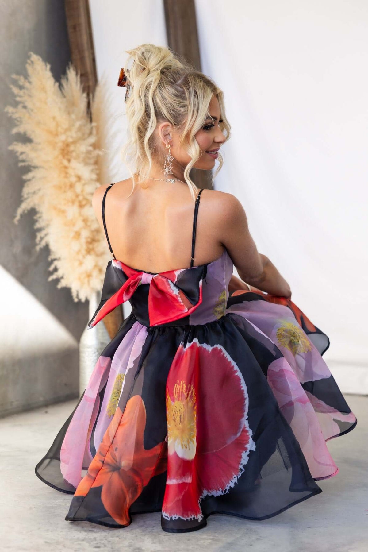 Back view of woman in colorful Rosebud Dress with floral print, adjustable straps, and a bow tie detail.