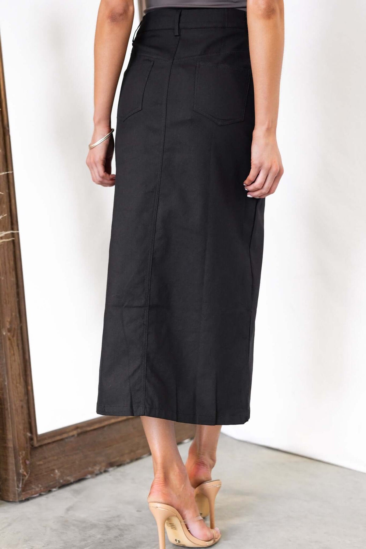 Back view of a woman wearing a black midi skirt with pockets and a mid-high waist fit.