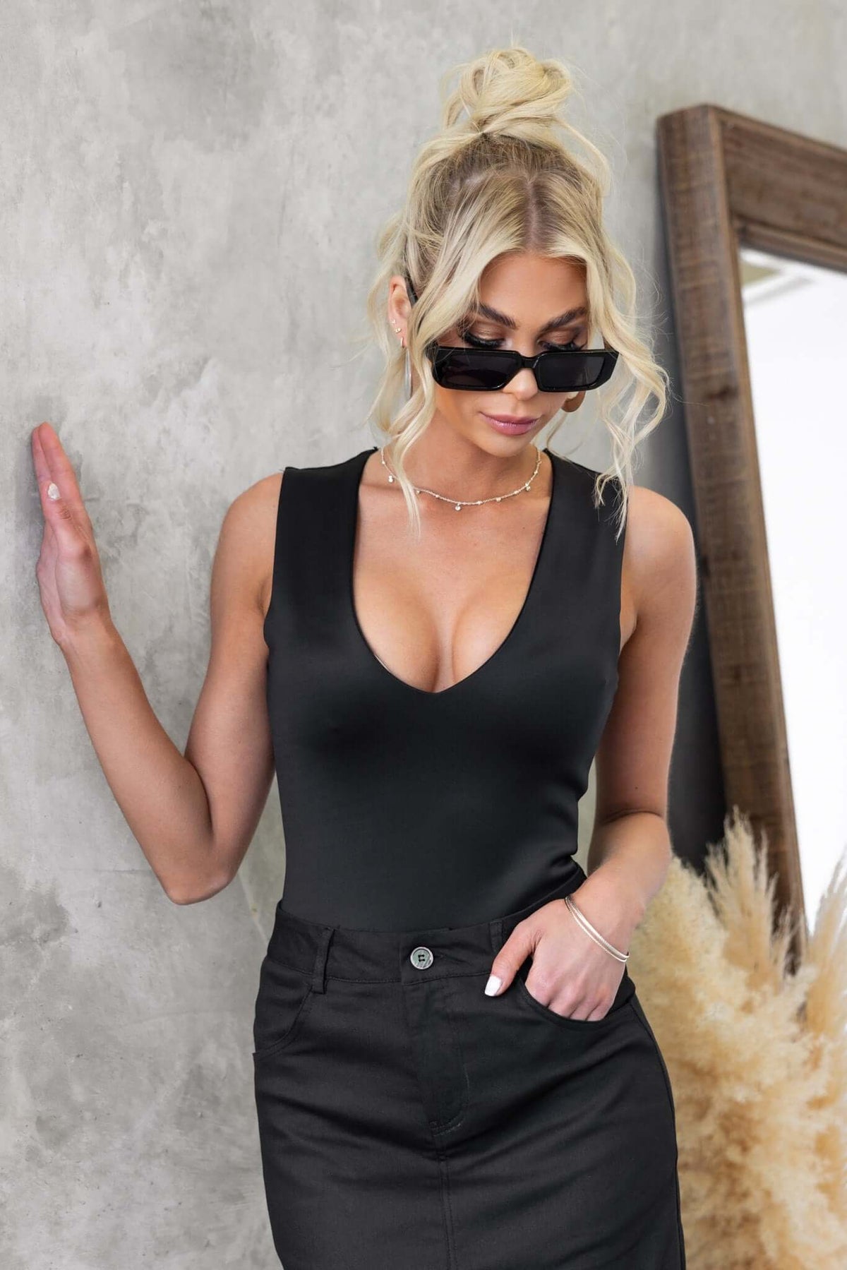 Model wearing a black Jenna Bodysuit with V-neckline, styled with sunglasses and a high-waisted skirt.