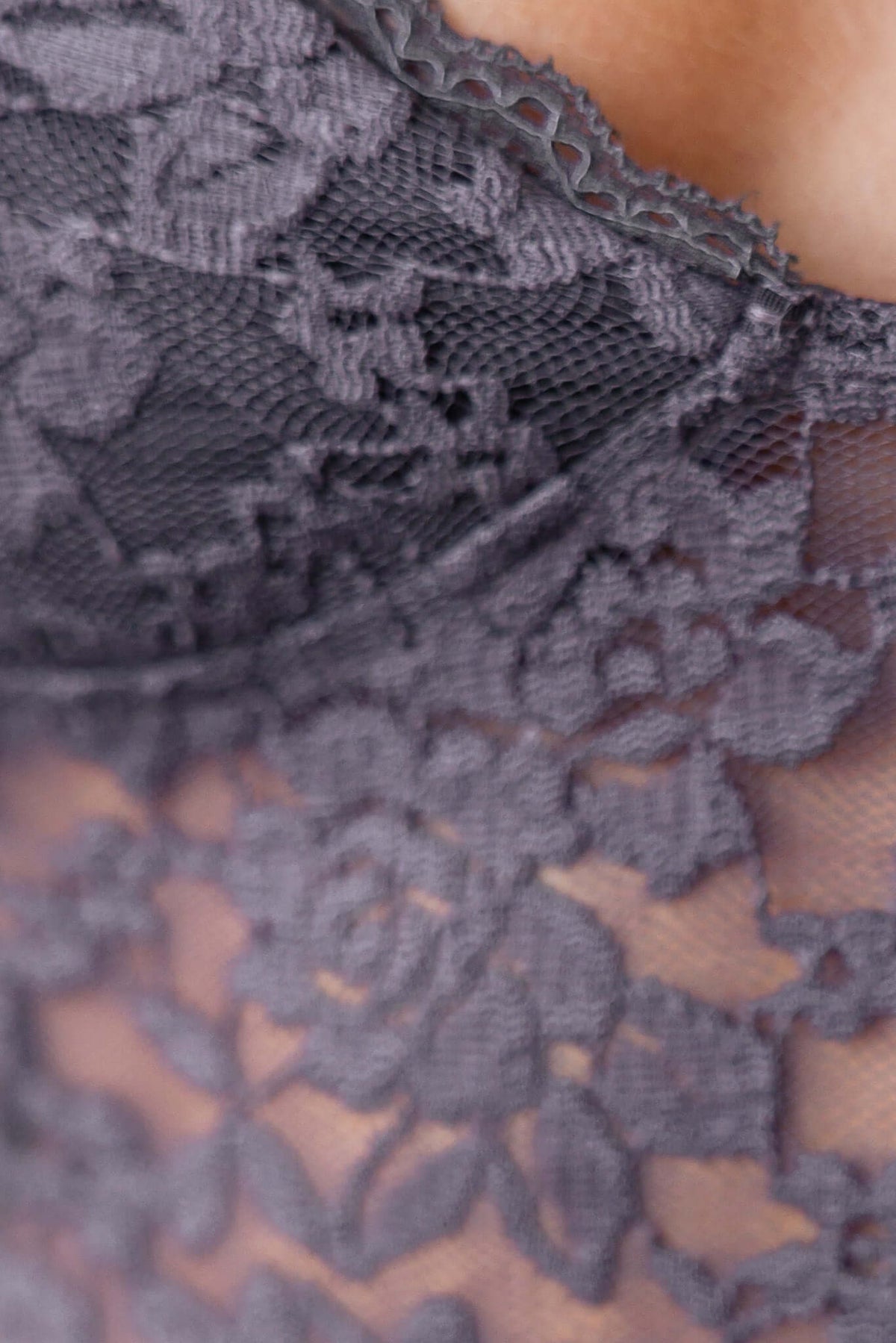 Close-up of a grey lace detail on a bodysuit, showcasing intricate floral patterns and soft texture.