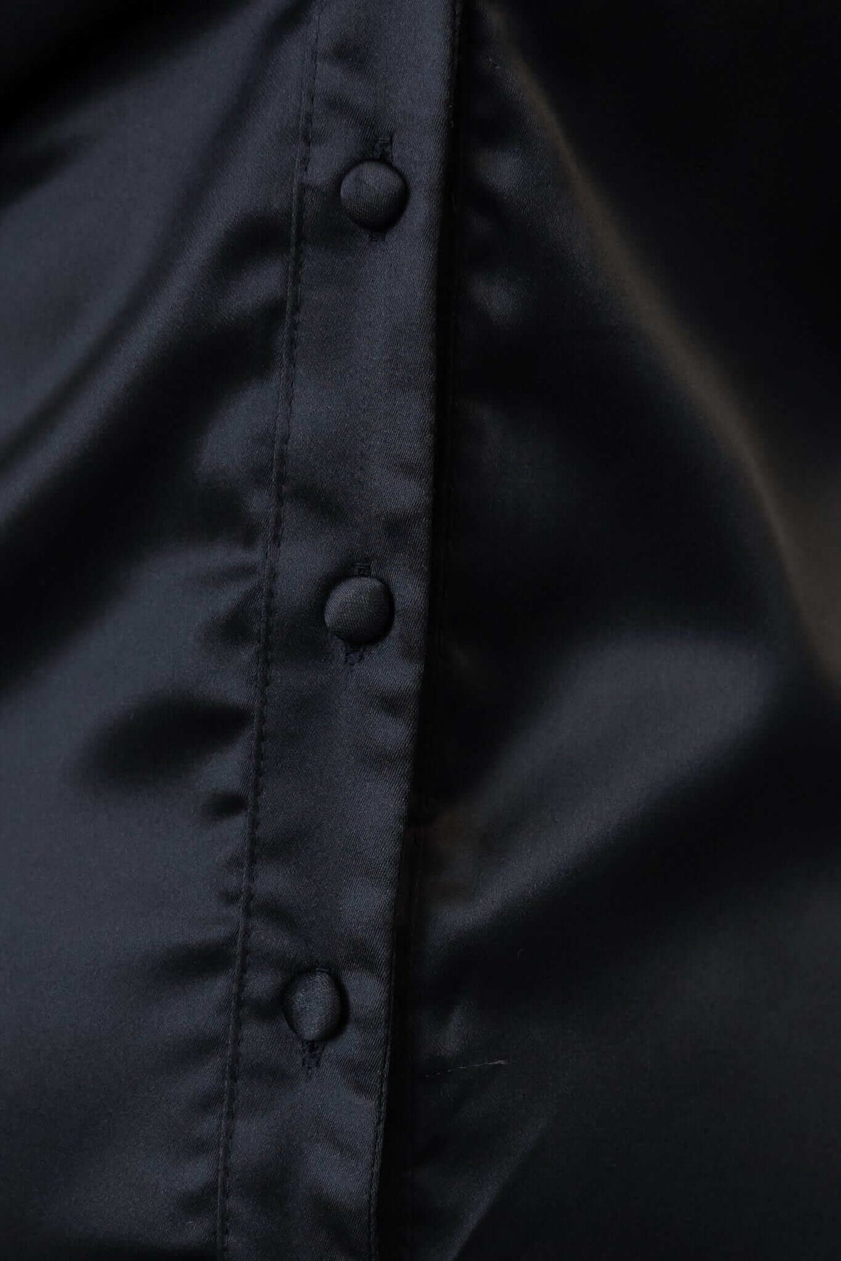 Close-up of black satin fabric showing button-up front details of the Findlay Dress.