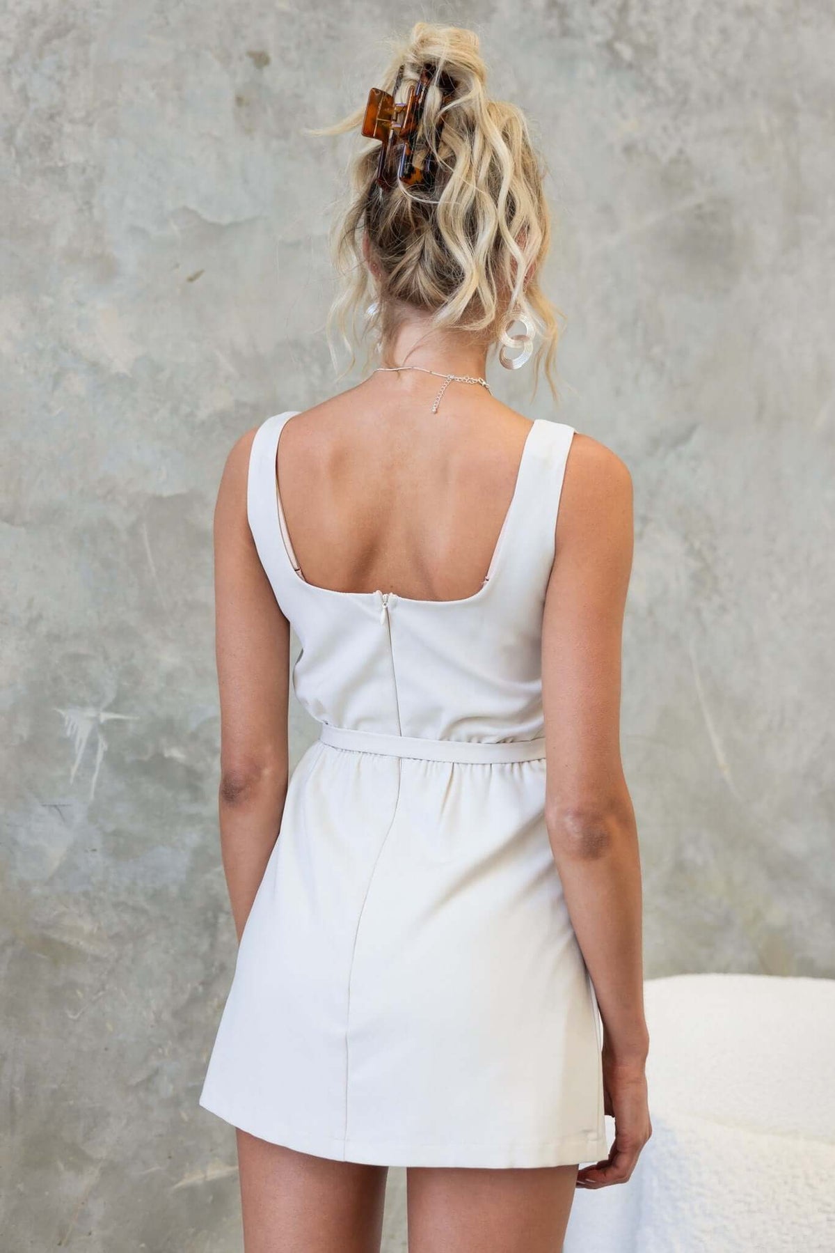 Back view of a woman wearing a Martel Playsuit, showcasing its wrap belt and invisible zip detail, styled with loose hair.