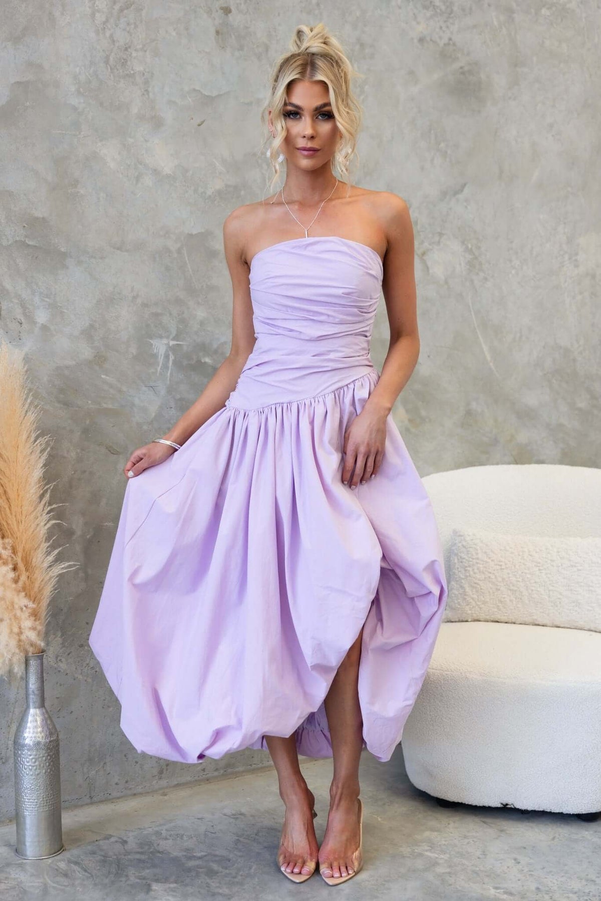Model wearing a lavender Carette midi dress with strapless design and asymmetric hemline.