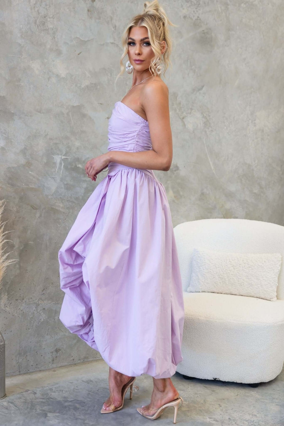 Model wearing the Carette Midi Dress in lavender, showcasing strapless design and asymmetric hemline.