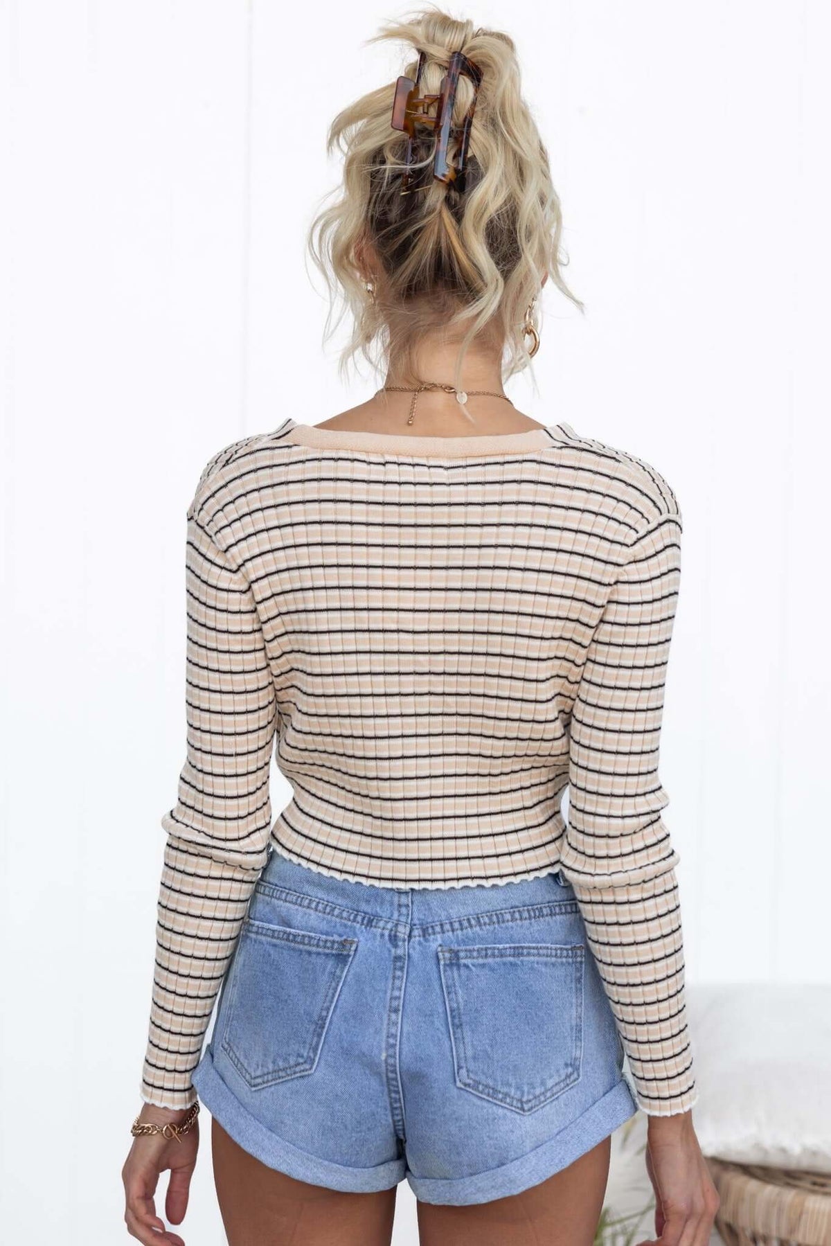 Back view of a woman wearing a ribbed striped Evan Top with long sleeves and denim shorts.