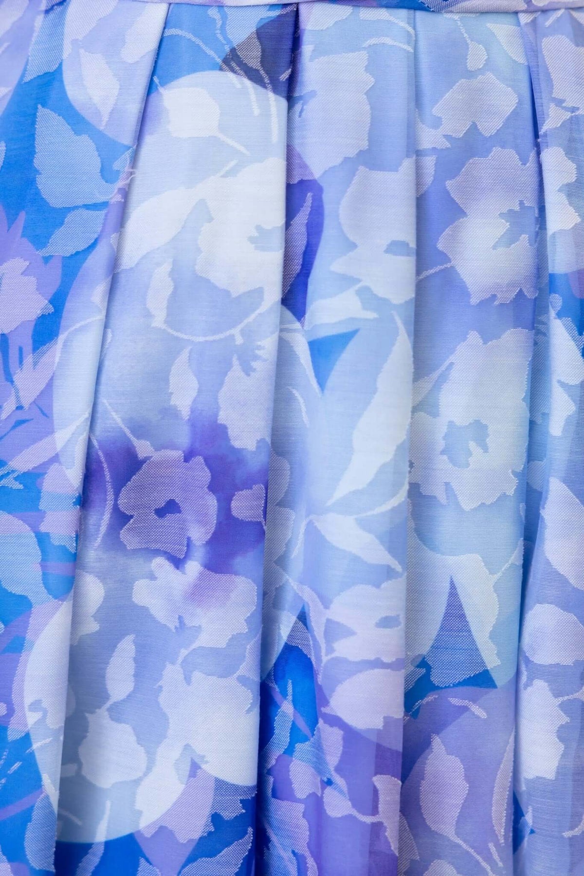 Close-up of silky blue floral fabric with pleats, showcasing a delicate pattern for a maxi dress.