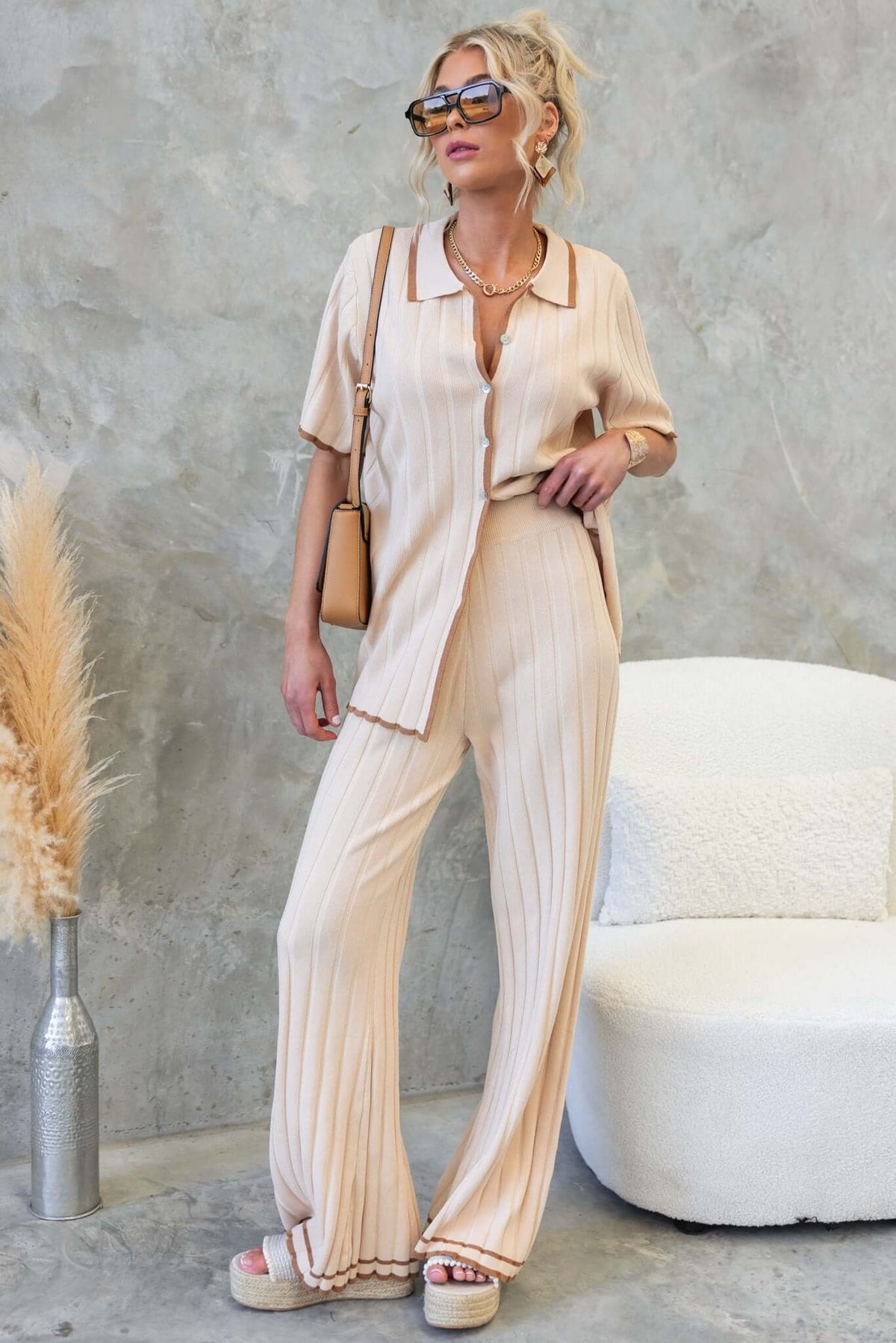 Stylish model in beige pleated pants and matching top, showcasing a chic summer outfit with sunglasses.