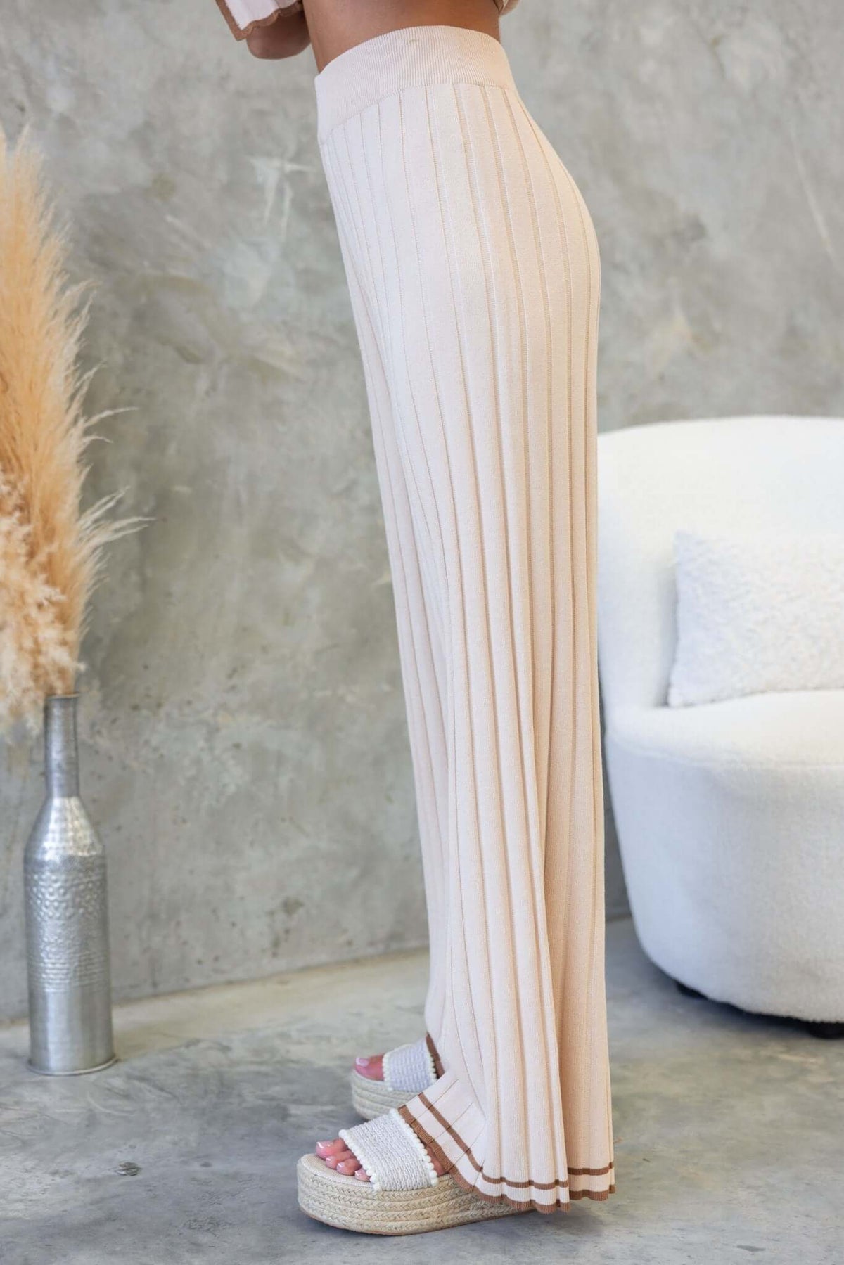 Side view of Jodie Pants, high-waisted ribbed knit pants in light beige with elastic waistband and pleated design.