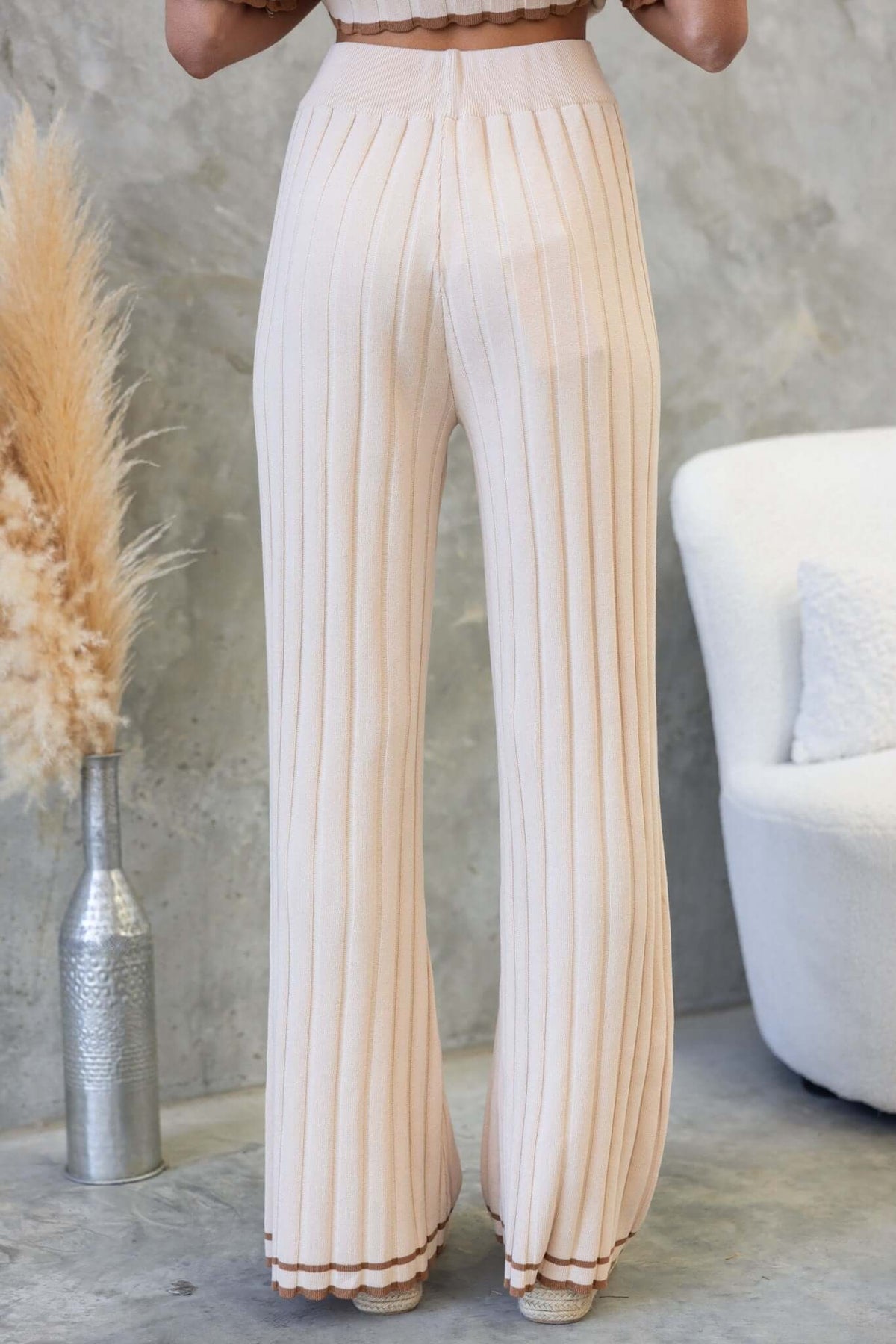Back view of cream-colored ribbed pants with a mid-high waist, featuring a relaxed fit and elastic waistband.