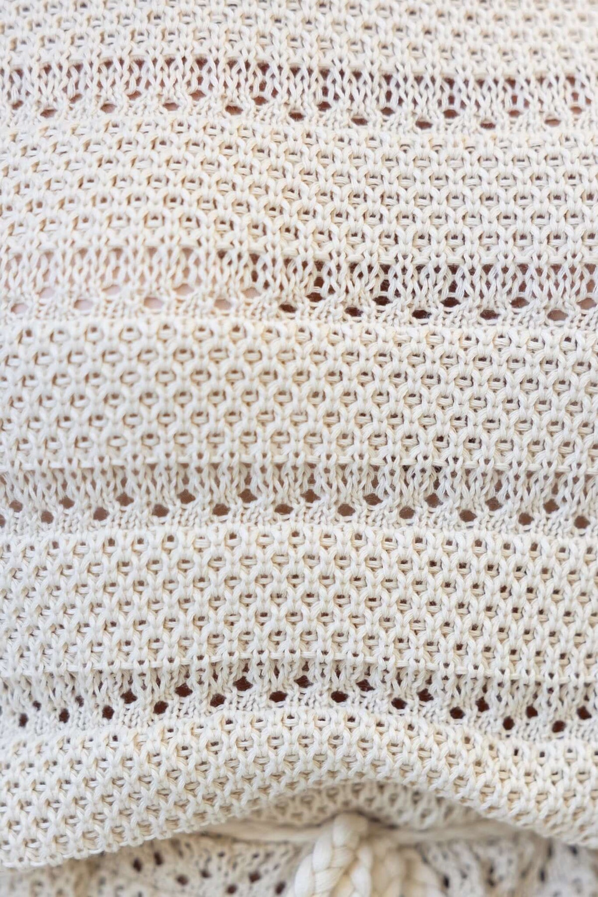 Close-up of crochet material in off-white color, showcasing intricate knit patterns and texture.