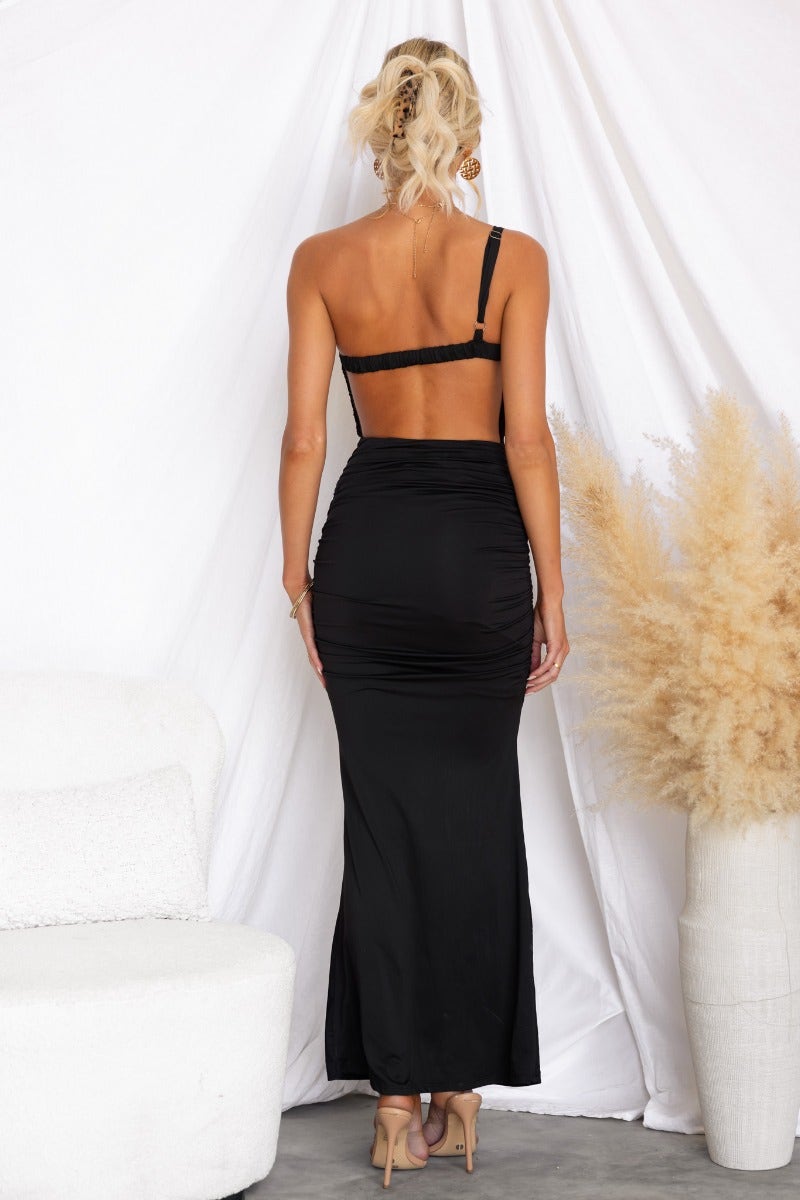 Back view of a woman in a black bodycon maxi dress with adjustable straps and ruched detailing.