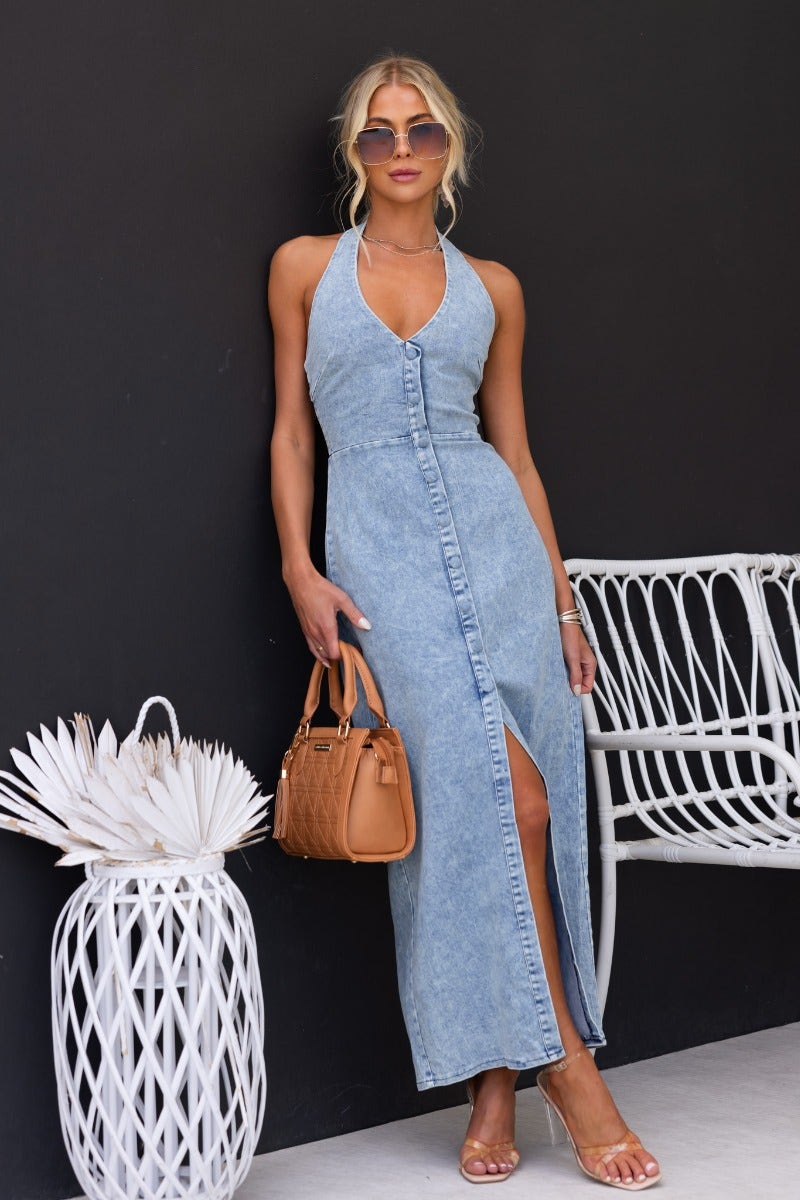 Yvette Denim Maxi Dress featuring a halter neckline, faux button-up front, and front split, styled with a handbag.