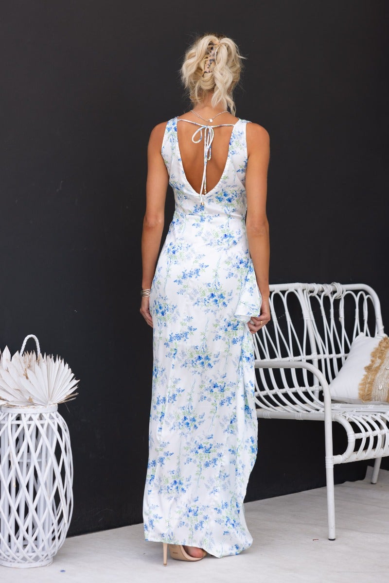 Back view of floral print maxi dress with tie detail, high neckline, and side ruffle, styled in a chic setting.