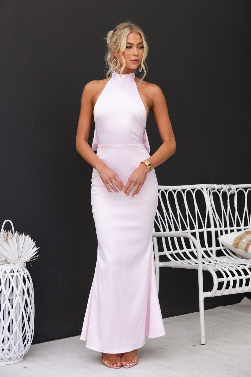 Model wearing a stunning pink maxi dress with high neckline and open back bow detail, perfect for elegant occasions.