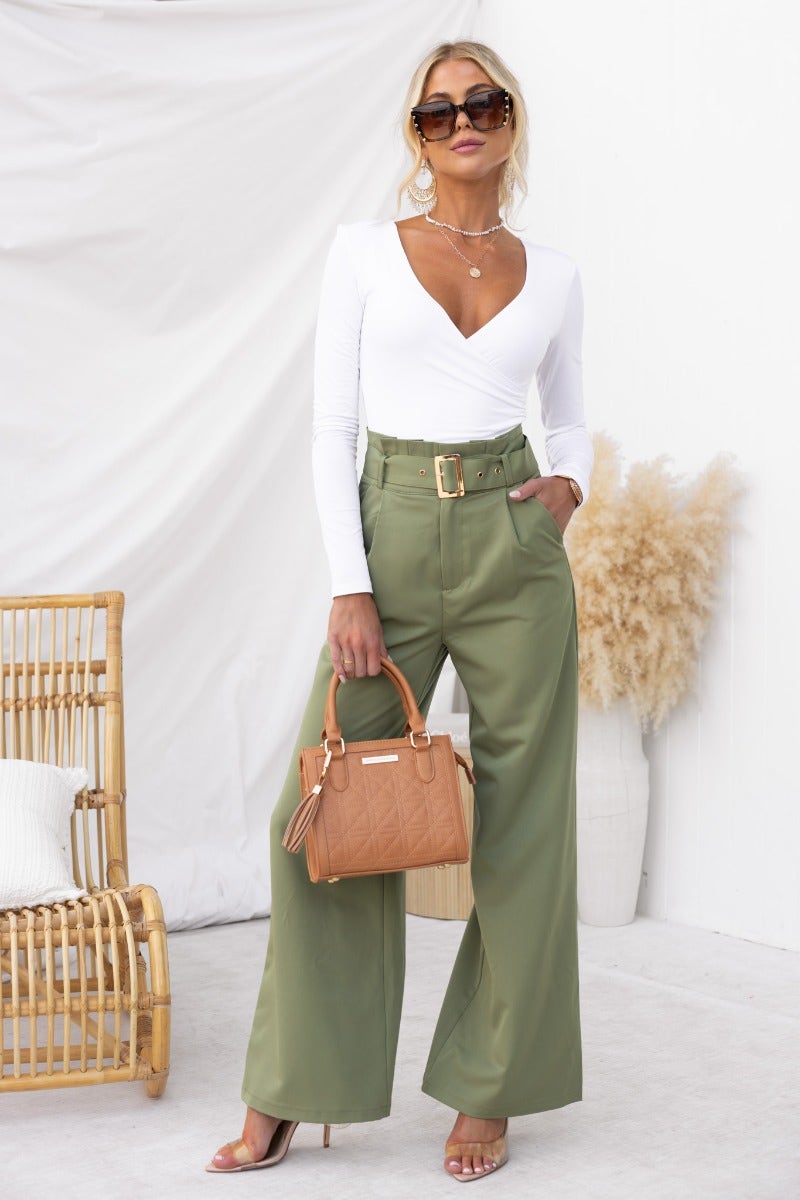 Stylish model wearing No Strings pants with paperbag waist, paired with a white top and carrying a brown handbag.