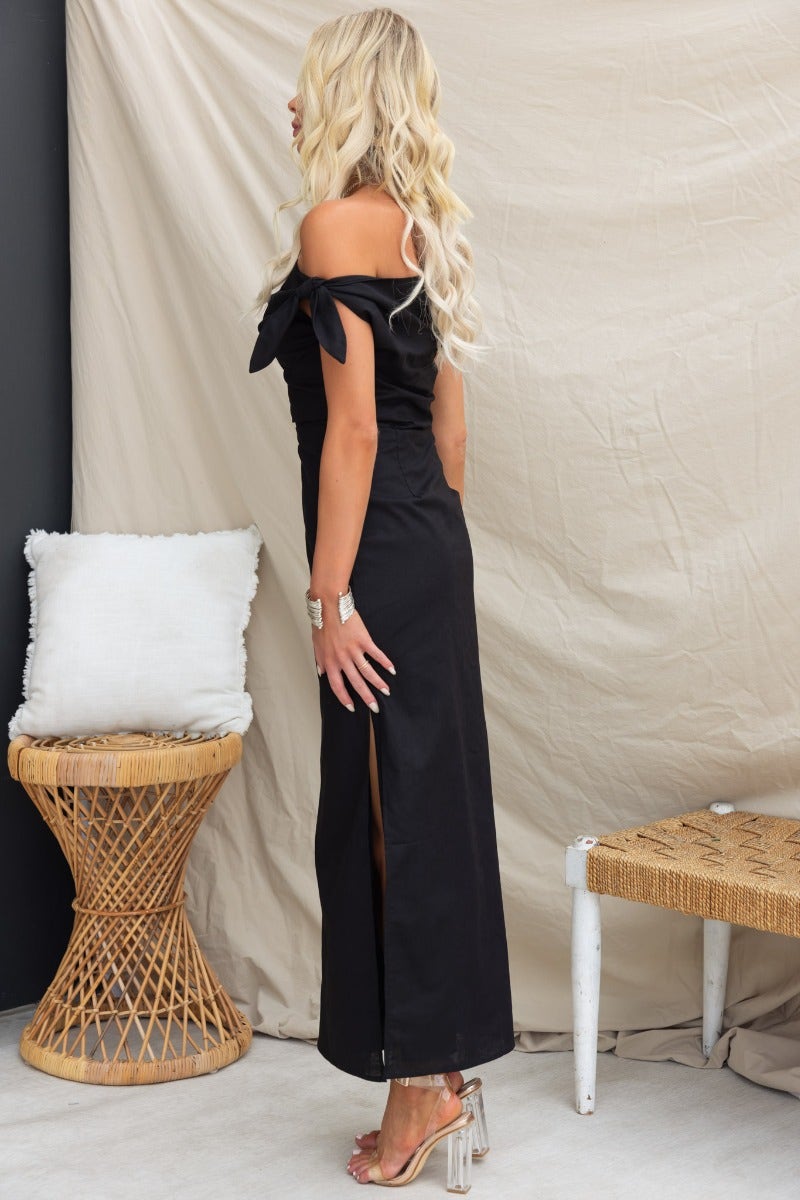 Side view of a black Annerly maxi dress with off-shoulder neckline and side split, styled with accessories.