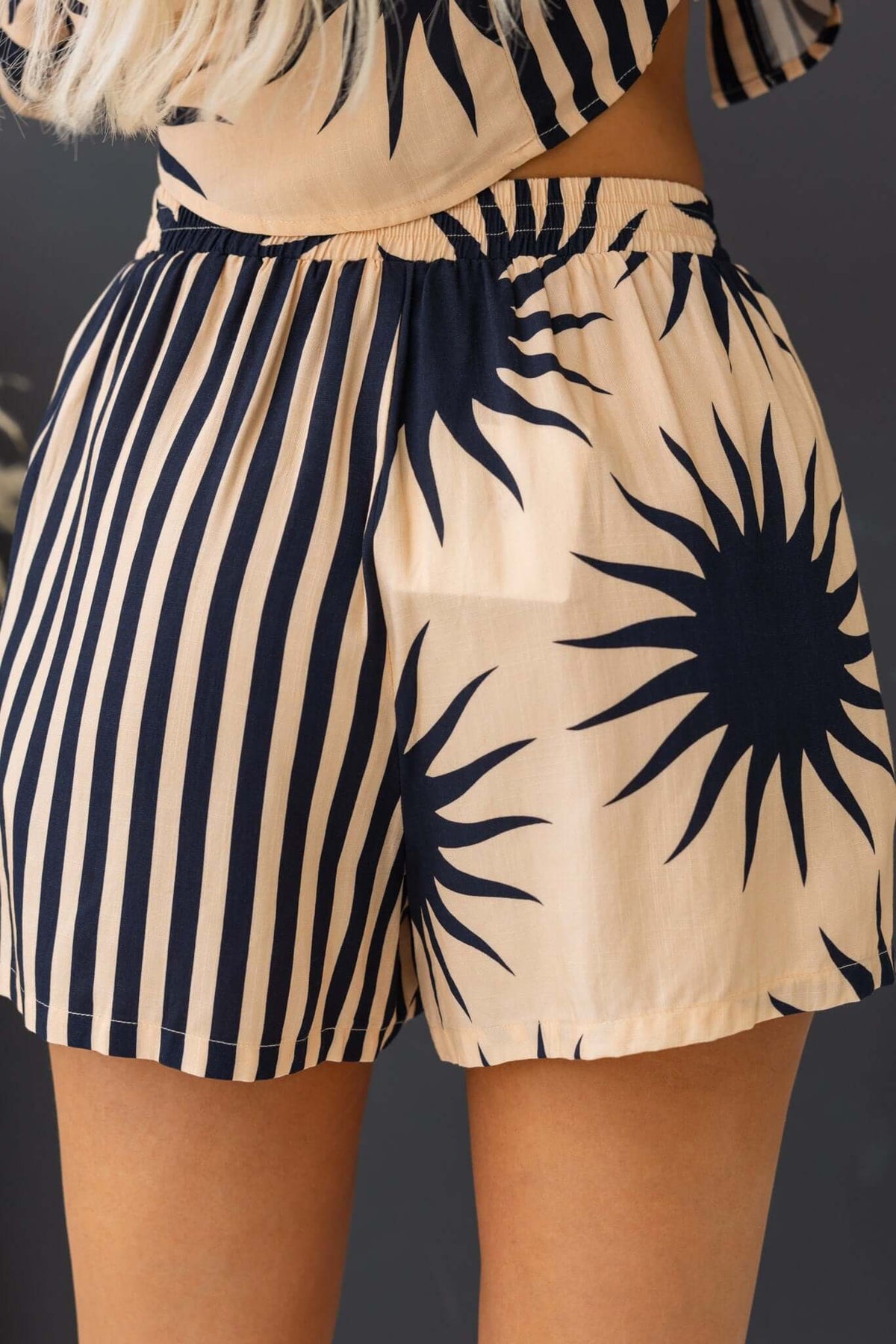 Back view of Hadley Shorts featuring a mid-high waist, elastic waistband, and sunburst pattern on a beige background.