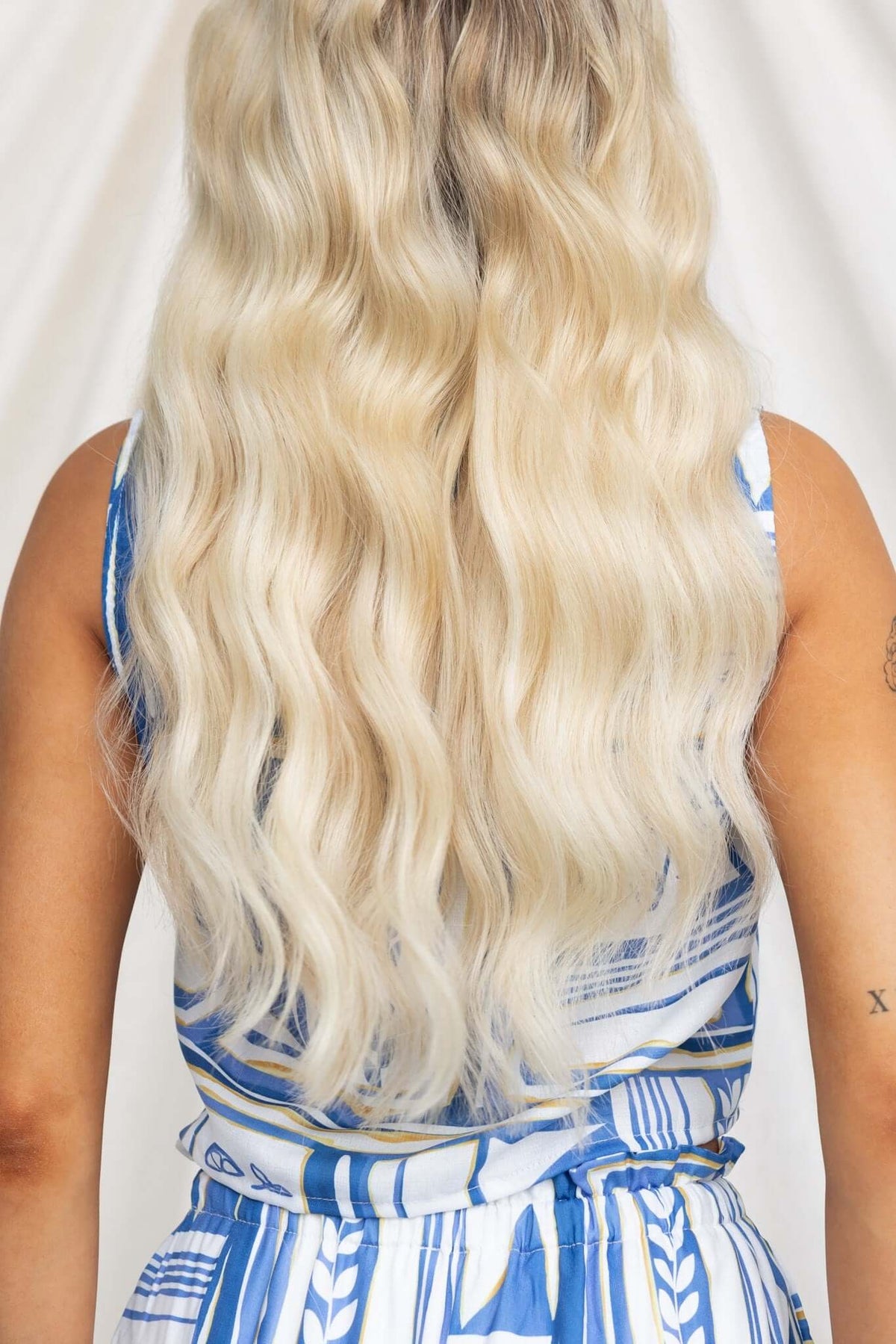 Back view of a woman with long blonde wavy hair wearing a blue patterned outfit.