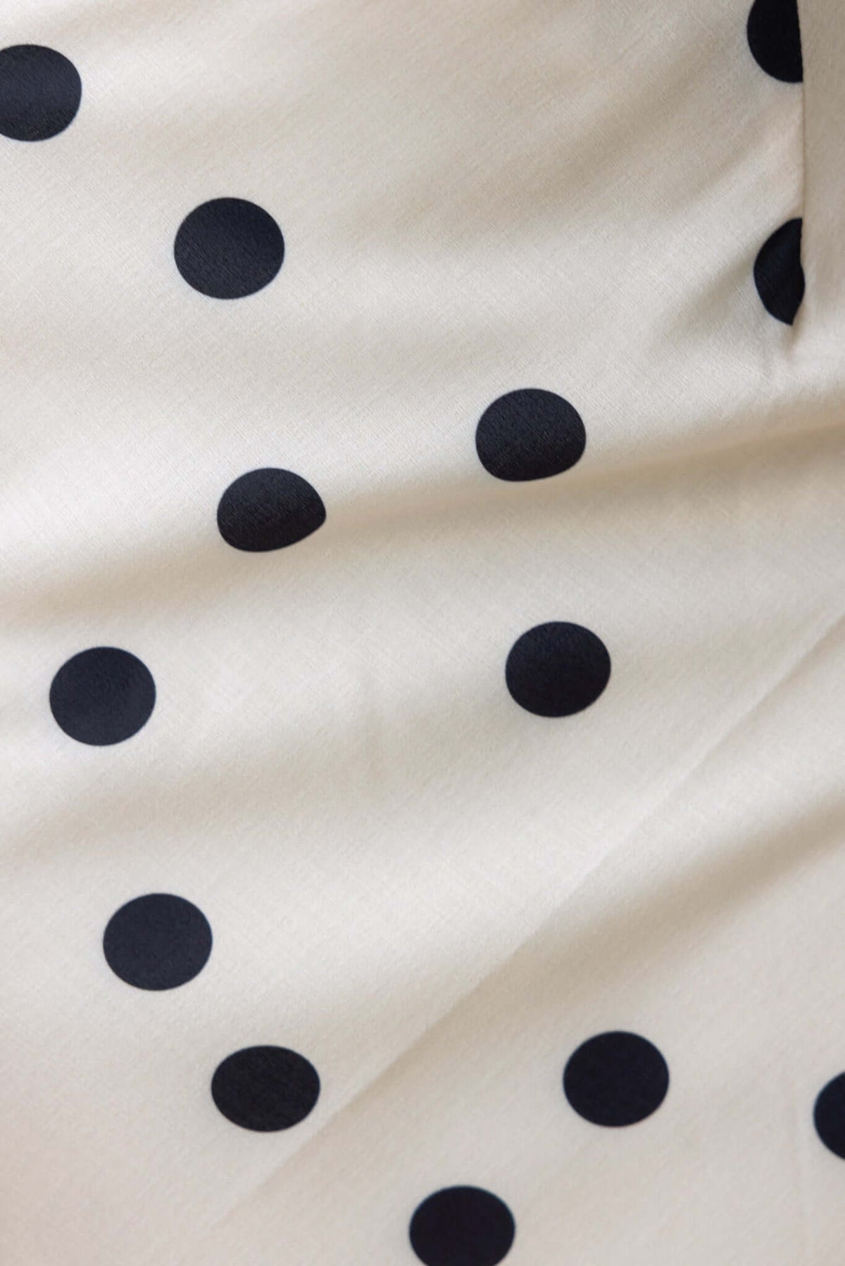 Cream fabric featuring large black polka dots, ideal for stylish apparel and accessories.