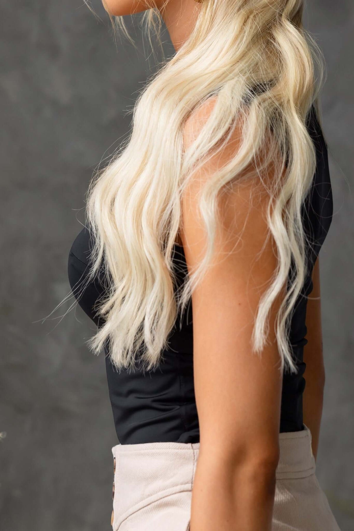 Side view of a model wearing a black square neckline top made of slinky material, showcasing long wavy blonde hair.