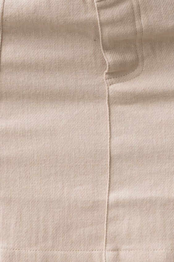 Close-up of a beige denim skirt showing stitching and pocket details, featuring a mid-high waist and non-lined design.