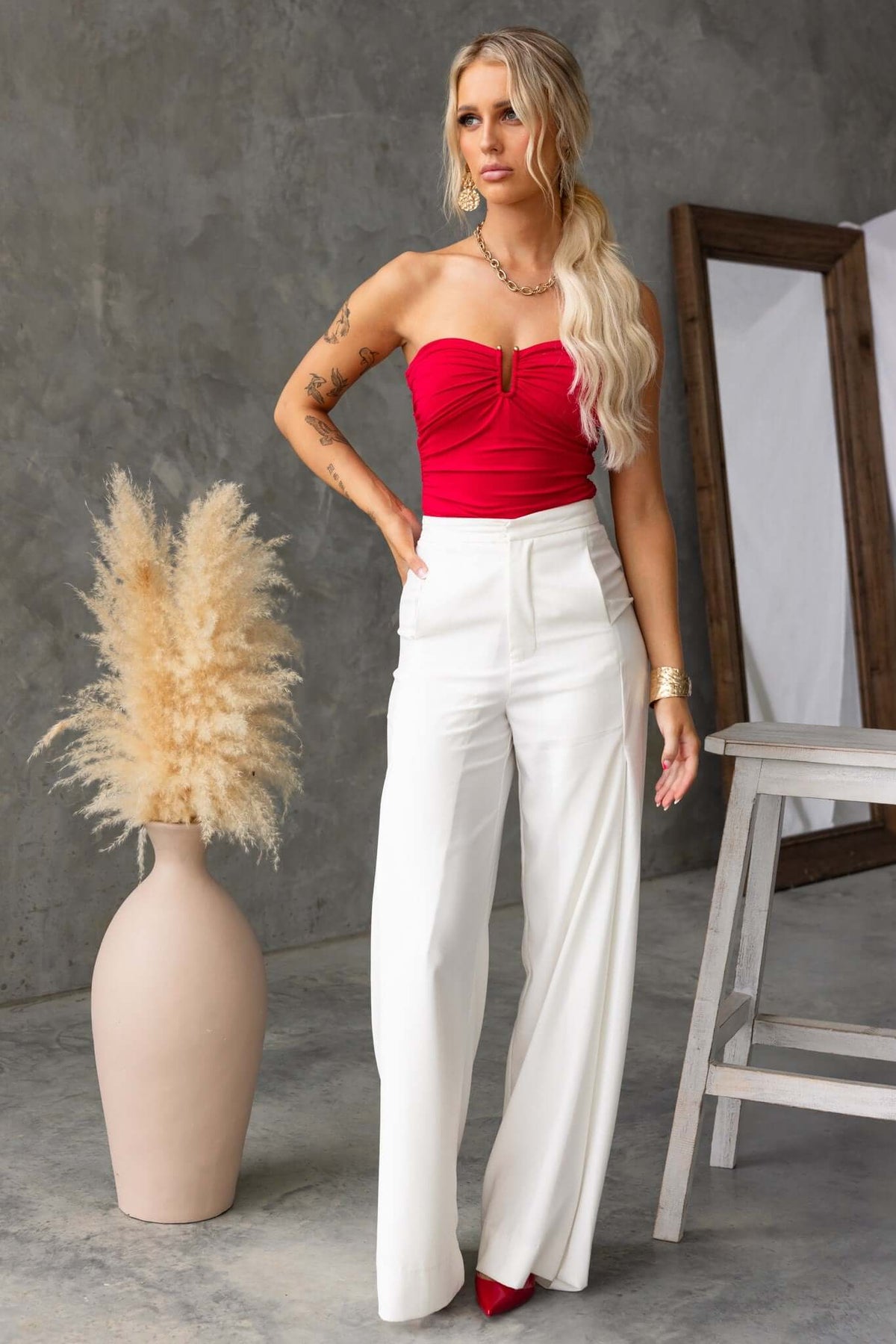 Model wearing an Ablaze strapless bodysuit with gold details and white high-waisted pants, styled in a modern setting.