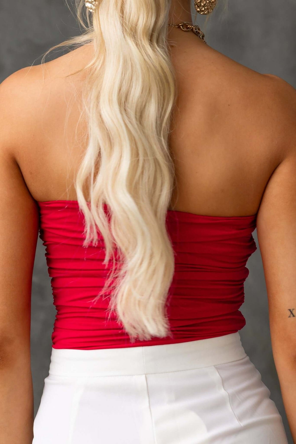 Back view of a woman in a strapless red bodysuit, showcasing its ruched design and blonde wavy hair.