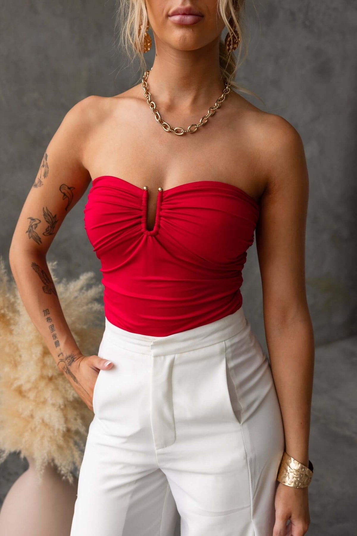 Strapless Ablaze Bodysuit in red with gold hardware detail, styled with high-waisted pants and accessories.