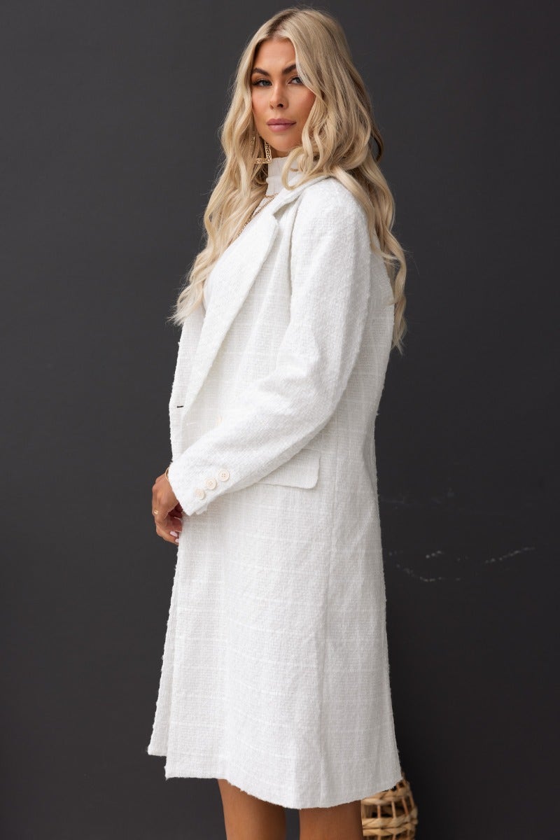 Model wearing the Zadie Coat, a longline white tweed coat with a collar, lapel, and button closure, featuring shoulder pads.